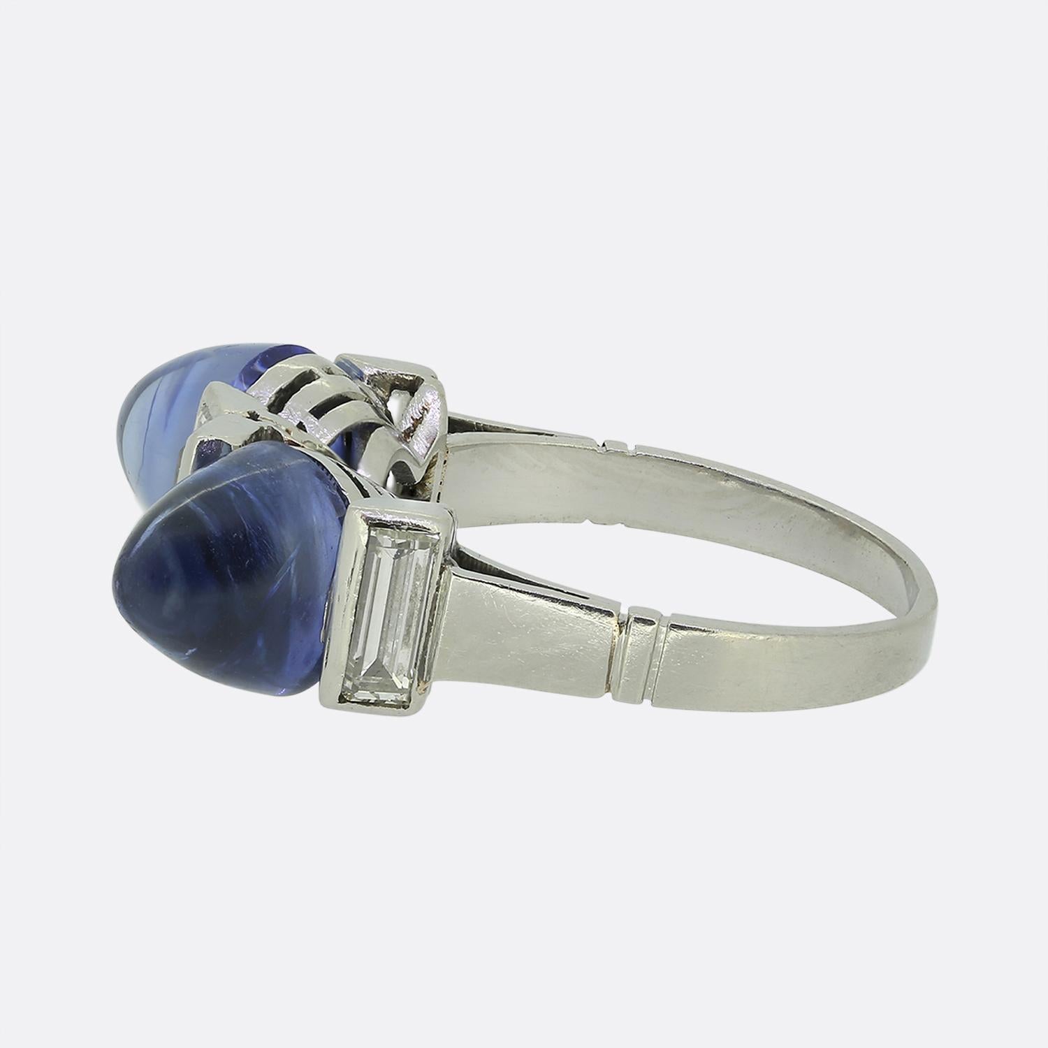 Here we have a true one-of-a-kind piece crafted during the pinnacle of the Art Deco movement. This platinum ring presents two domineering sugarloaf sapphires at the centre of the face. The term sugarloaf means that the gem has a conical shape with