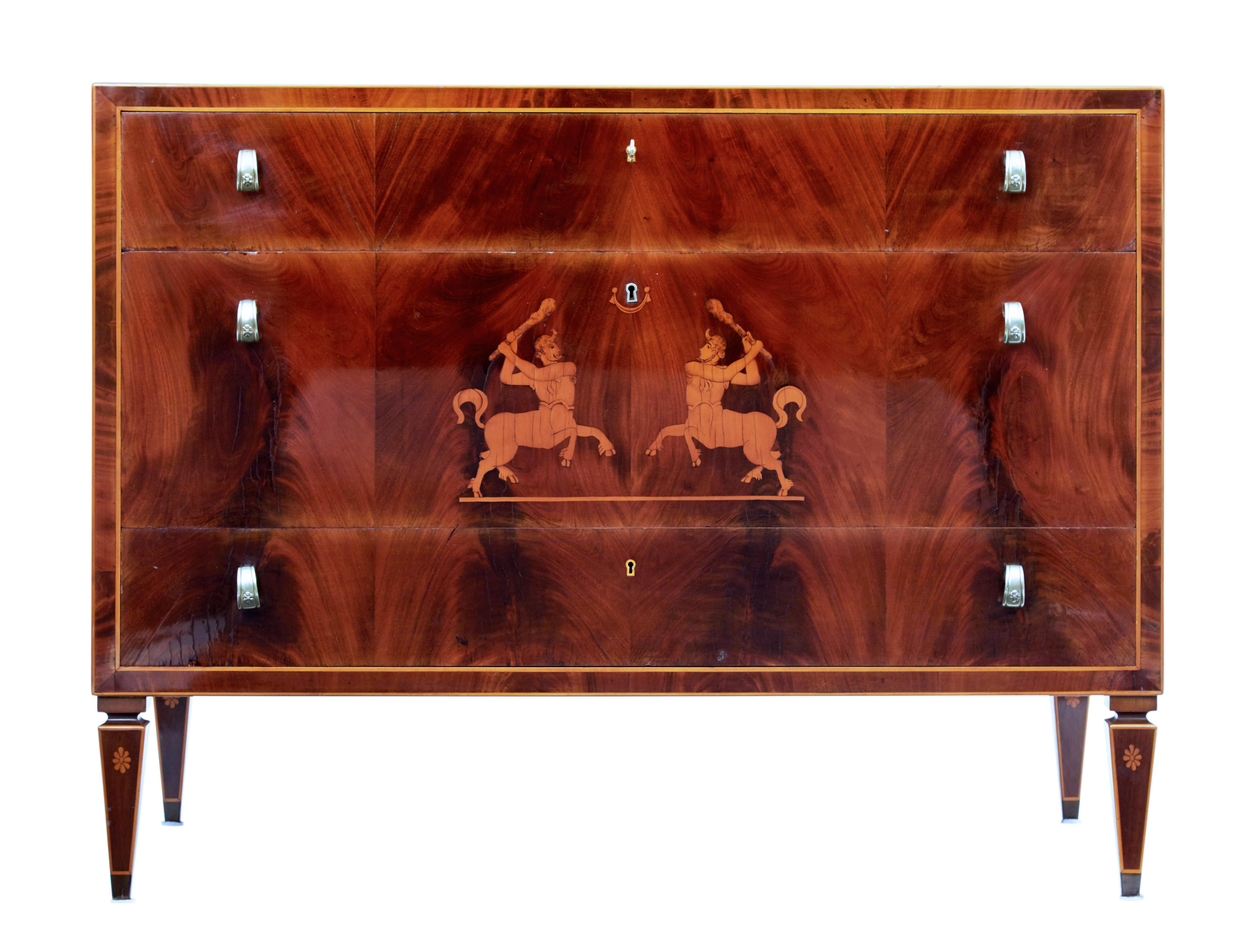 Stunning period Art Deco chest of drawers circa 1931.

Flame mahogany top surface with crossbanding and stringing. 3 drawers to the front of varying depth. Middle drawer with inlaid battling centaurs. Decorative looped handles.

Oak lined