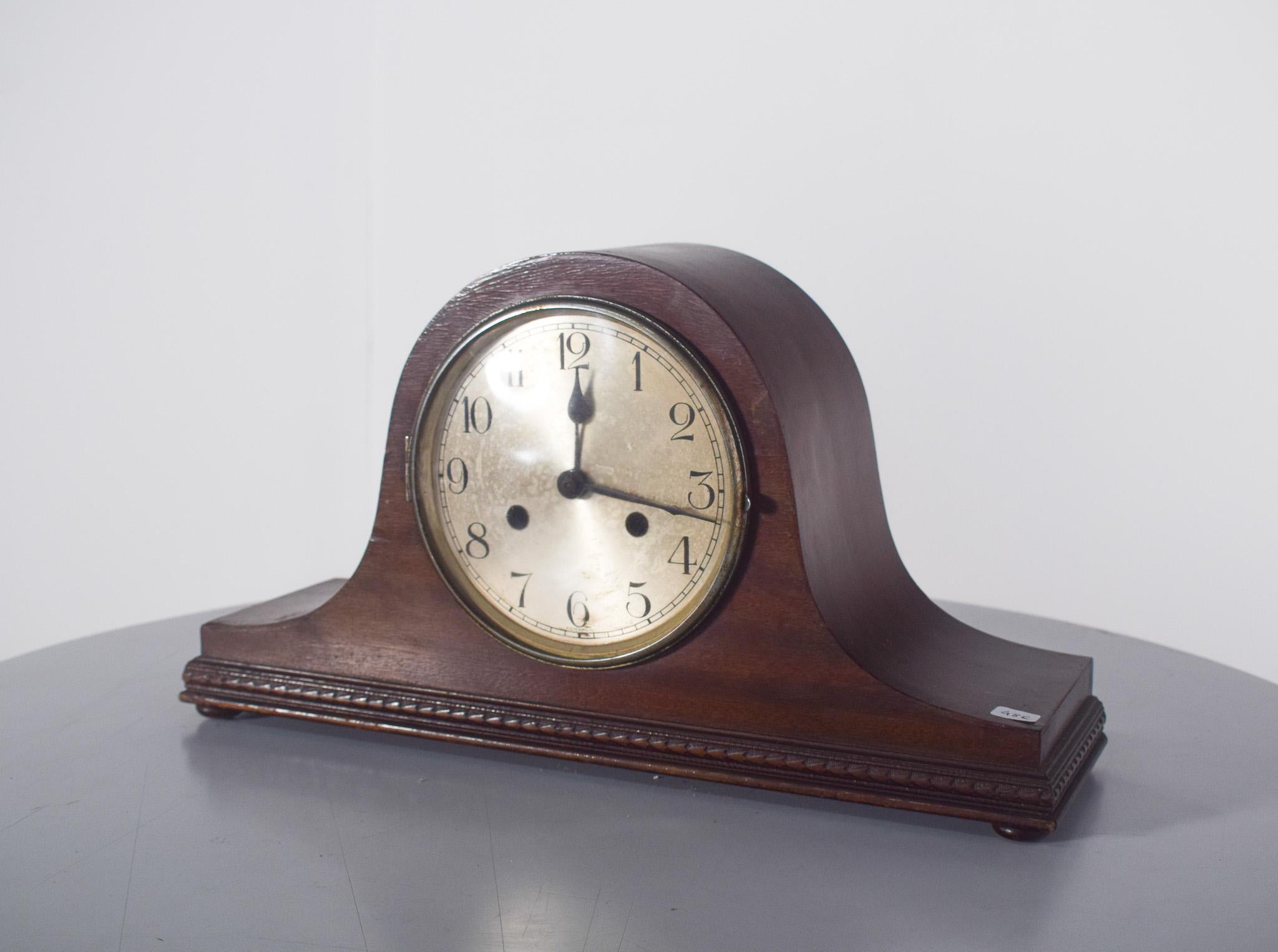 Art Deco table clock. With a dark wood frame, it has a classic dome-shaped design, very popular at the beginning of the 20th century, with a solid base decorated with a carved frieze.
The circular dial has an aged metal background, with Arabic