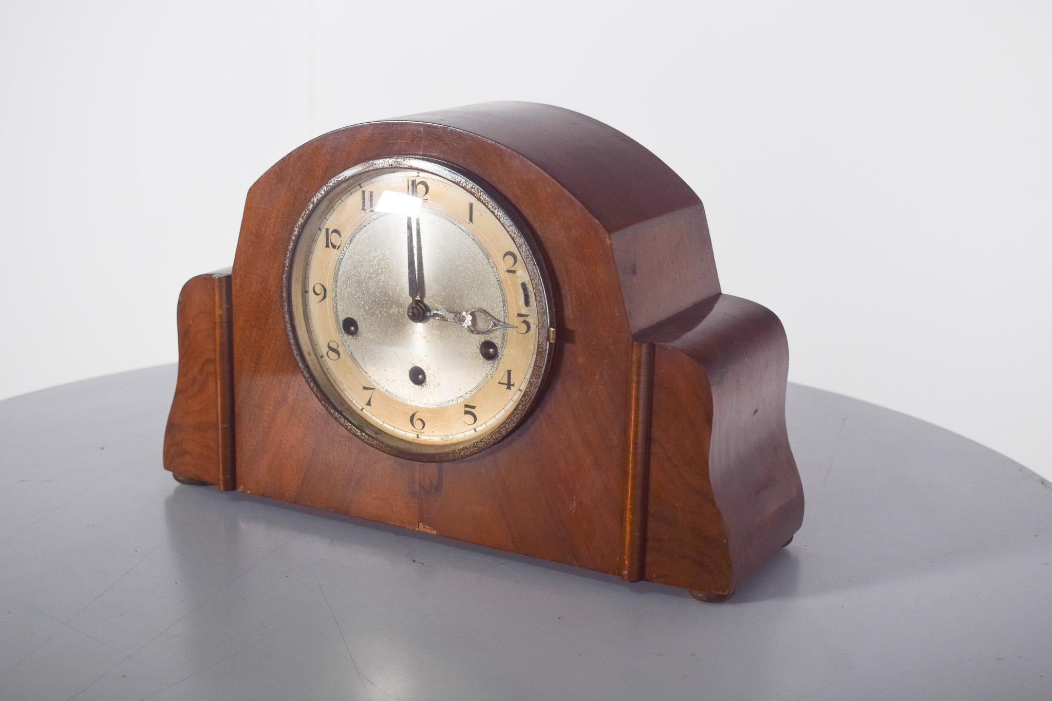Horloge de table Art Déco. Doté d'un cadre en bois clair, il présente un design géométrique équilibré avec des courbes douces et des détails latéraux discrets
Le cadran circulaire présente un fond en métal vieilli avec des chiffres arabes et des