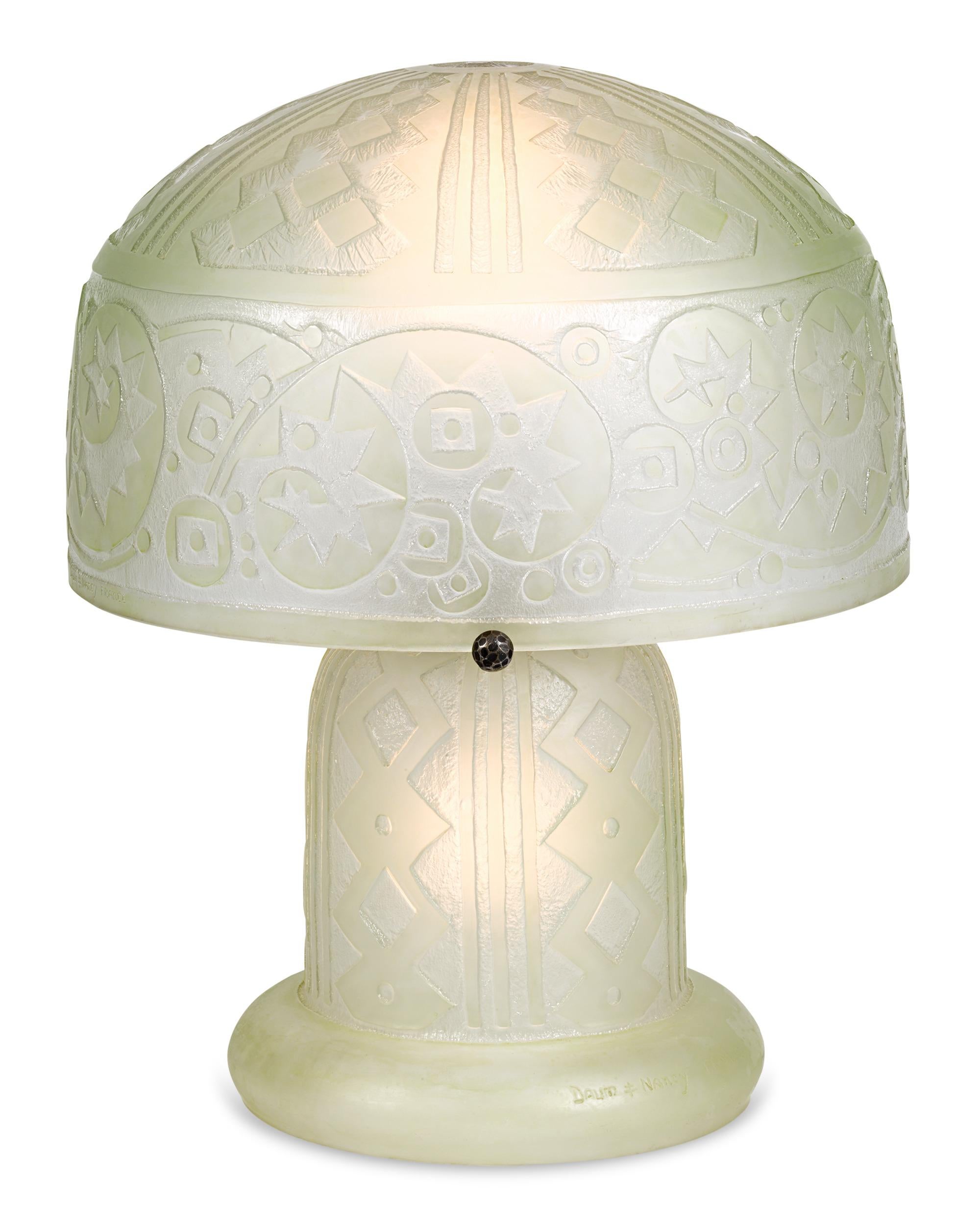 Exemplary of the finest in Art Deco glass design, this acid-etched table lamp is handcrafted by the pioneering glassmaker Daum Nancy. The thick glass of both the upper shade is heavily ornamented with stylized, geometric forms, accented by handmade