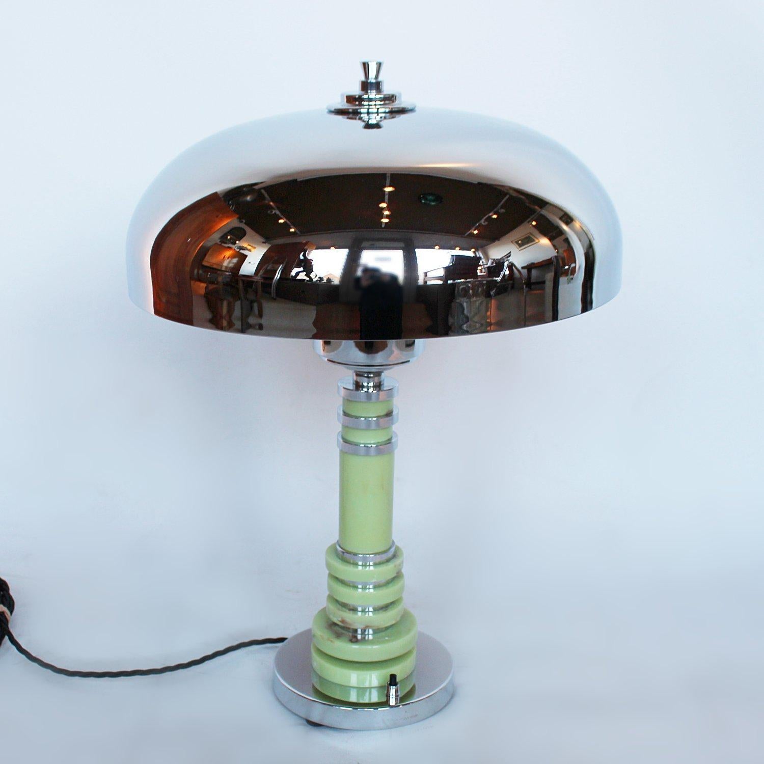 A tall Art Deco table lamp with a domed shade. Tubular, mint coloured bakelite stem with bands of chromed metal and alternating discs of bakelite and chromed metal. Set over a flat base. Metal finial to top.

Fully refurbished, re-chromed and