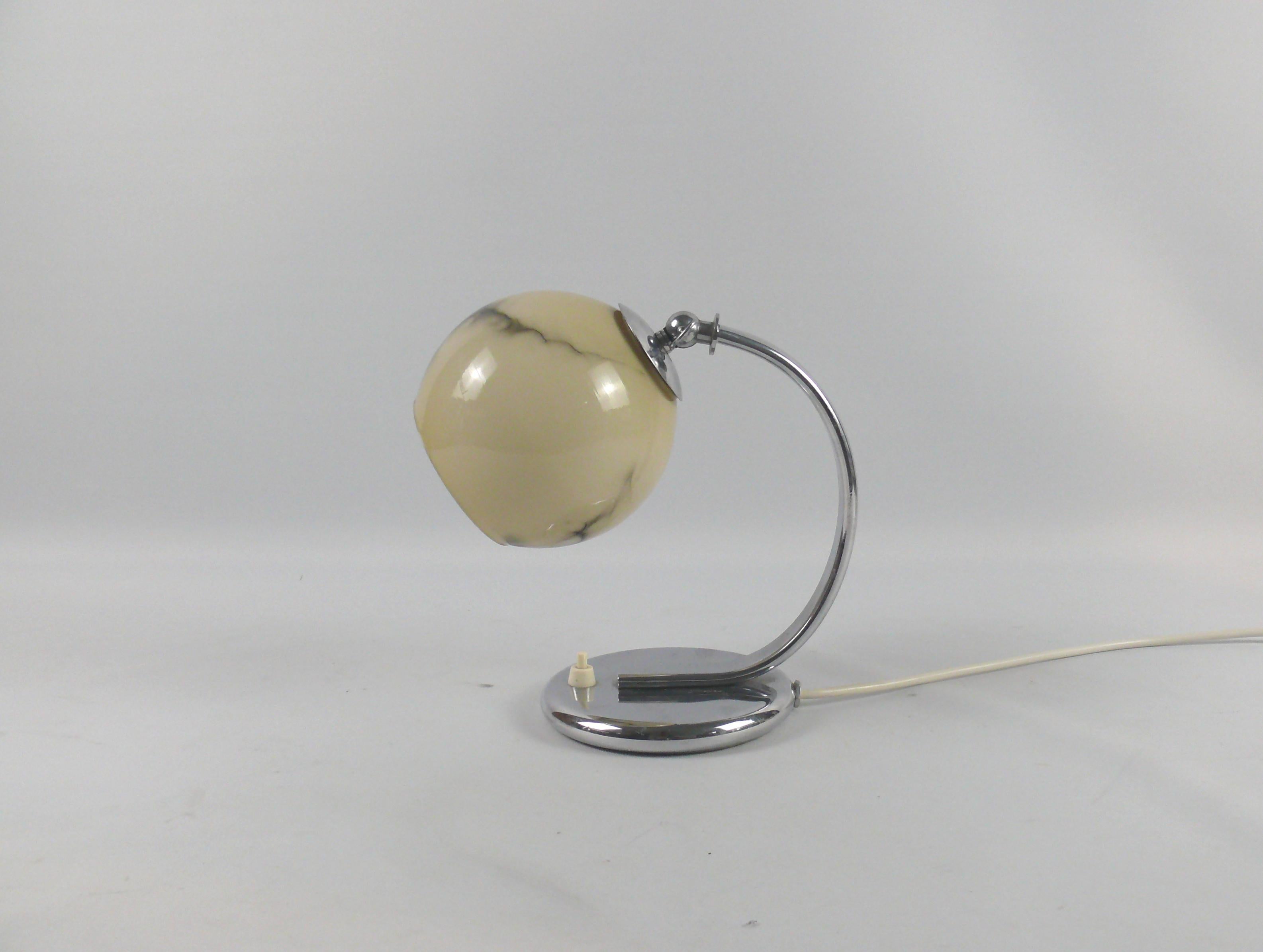 Mid century table lamp, probably from the 1930s - 1950s in good condition. The lamp impresses with its shiny chrome-plated round base and the decorative, marbled shade. The lamp is equipped with an E 27 brass socket and the height of the shade can