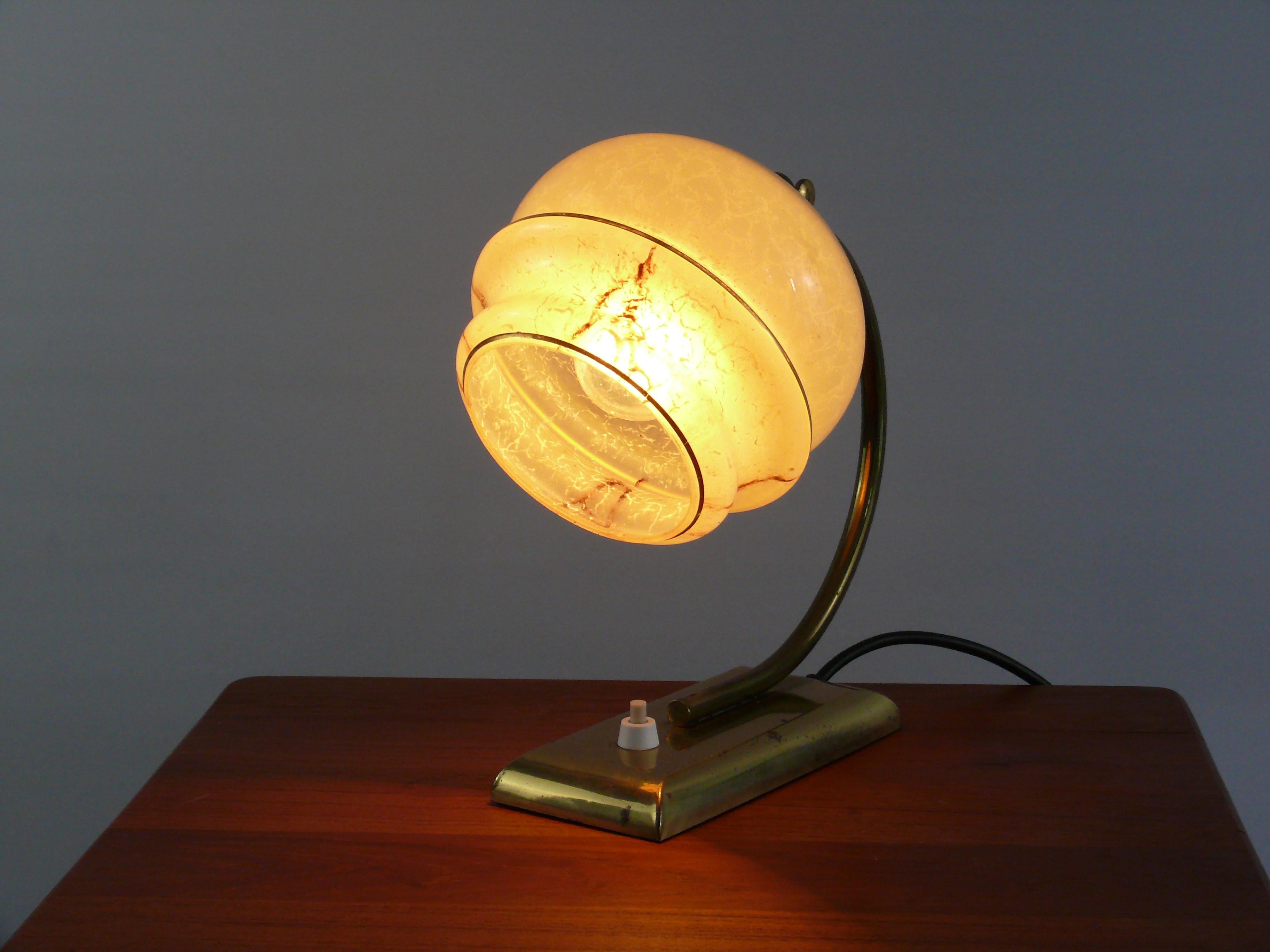 Well-preserved Art Deco table lamp from the 1930s - 1940s. The lamp is made of brass and has a yellow spherical shade with radial decorative stripes. The shade can be adjusted via a joint with a knurled screw. Some of the brass parts show dark