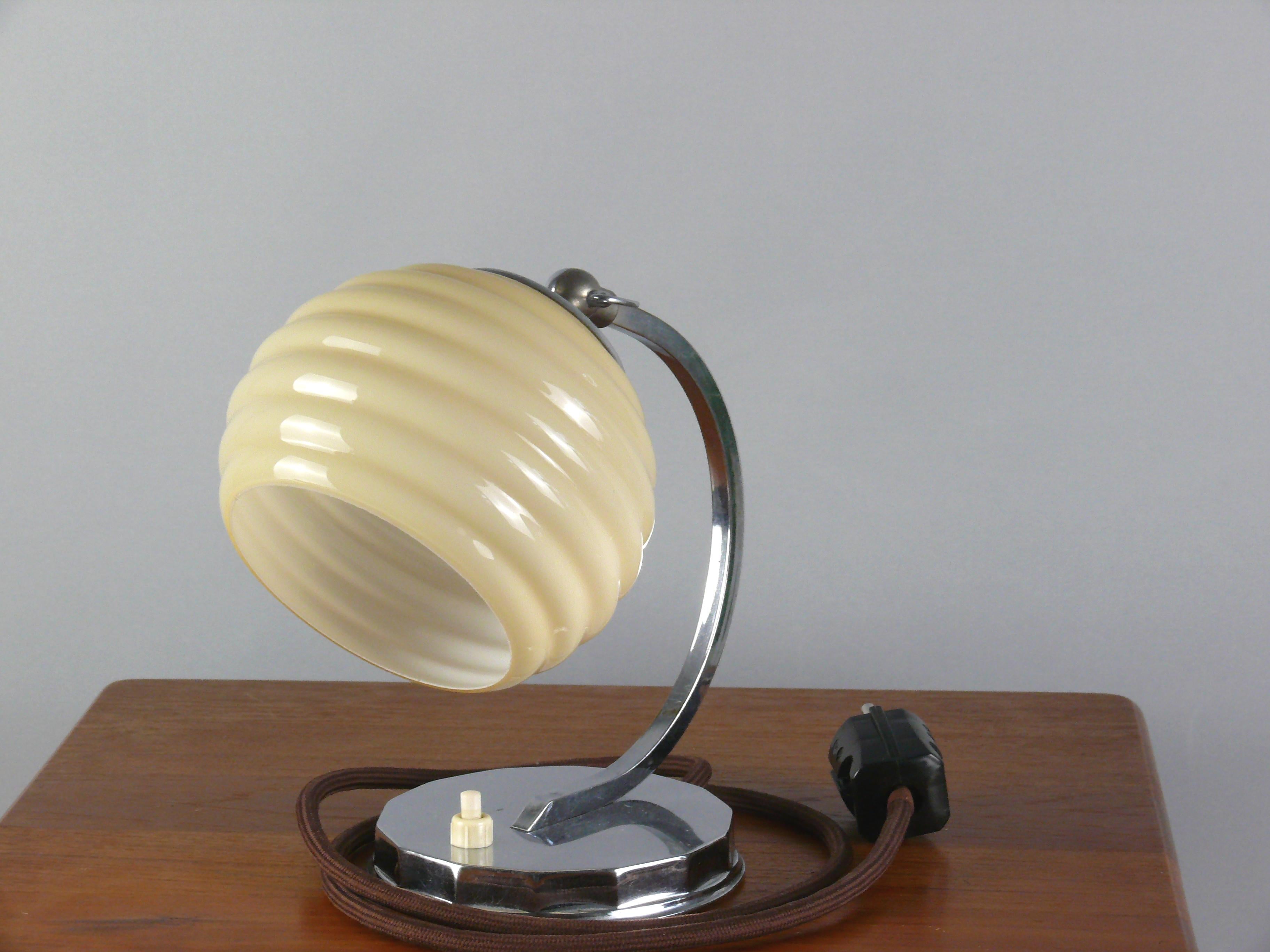 Art Deco Tischlampe, wahrscheinlich aus den 1930er Jahren in gutem Zustand. Die Leuchte besticht durch ihren glänzend verchromten Rundsockel und den dekorativen Schirm. Die Lampe ist mit einer Messingfassung E 27 ausgestattet und der Schirm kann mit