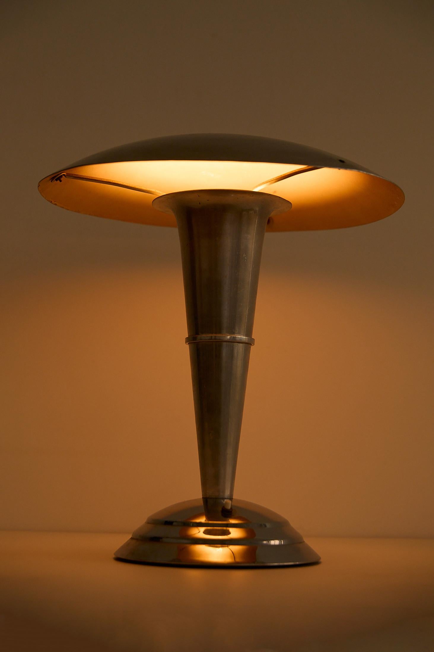 Art Deco table lamp, France, circa 1930s. Made of chromed metal, it features a wide circular shade, tapered conical stem, and stepped round base. The lamp’s clean geometry and polished finish reflect the refined elegance and modernity characteristic