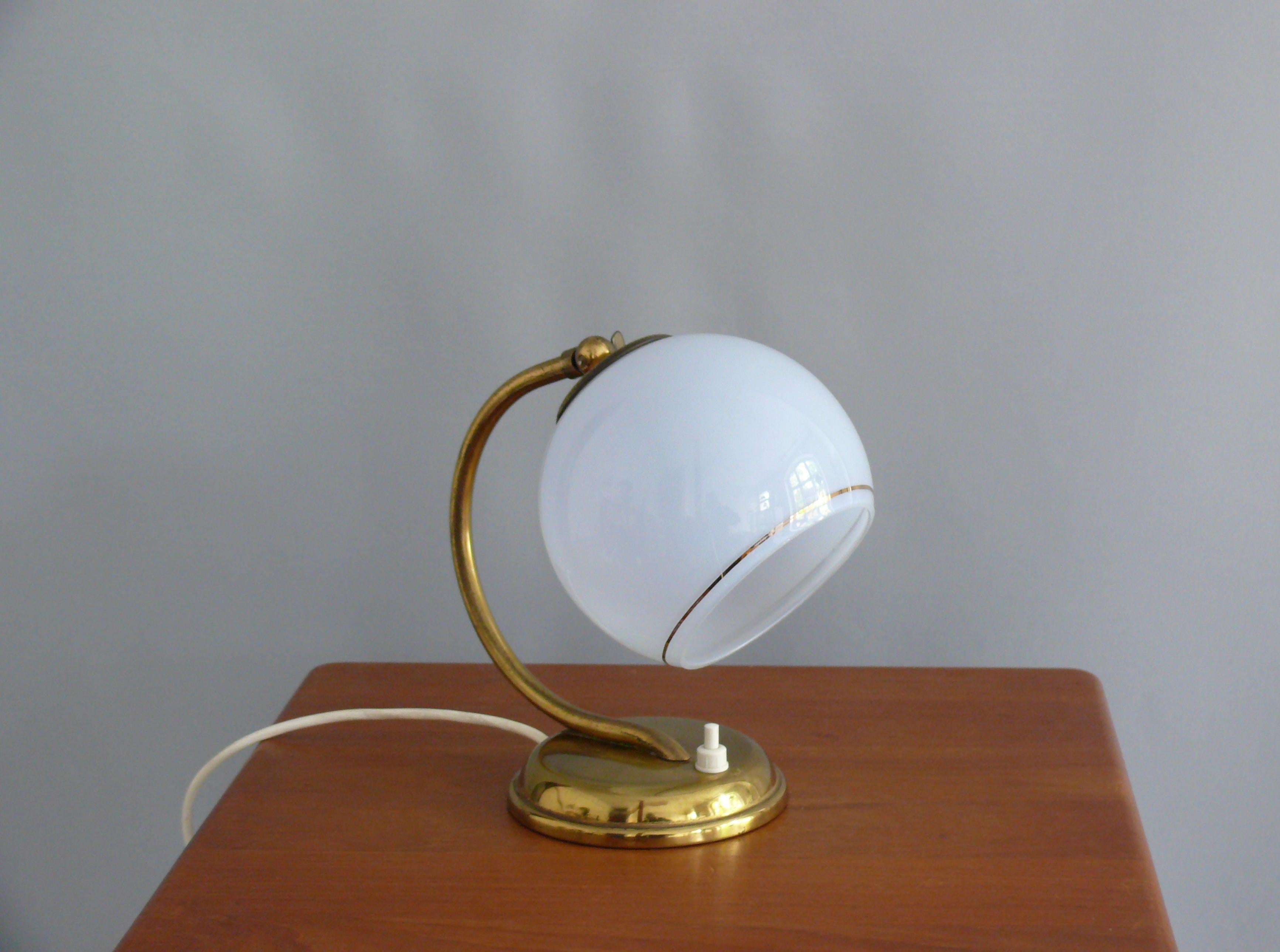 Vintage table lamp from the 1930s to 1950s in good condition. The lamp is made of brass and has a light blue, spherical glass shade. The shade is in good condition, can be adjusted via a joint with a wing screw, and has a golden radial decorative