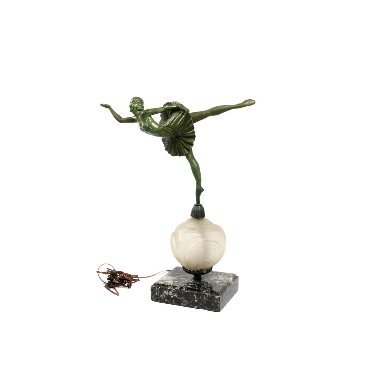 Lampe de table Art déco avec statue : Une figure en métal vert émeraude représentant une danseuse en pleine extension, dansant sur un pied. Elle est posée sur un globe en verre dépoli qui diffuse une lumière douce, soutenu par une base en marbre