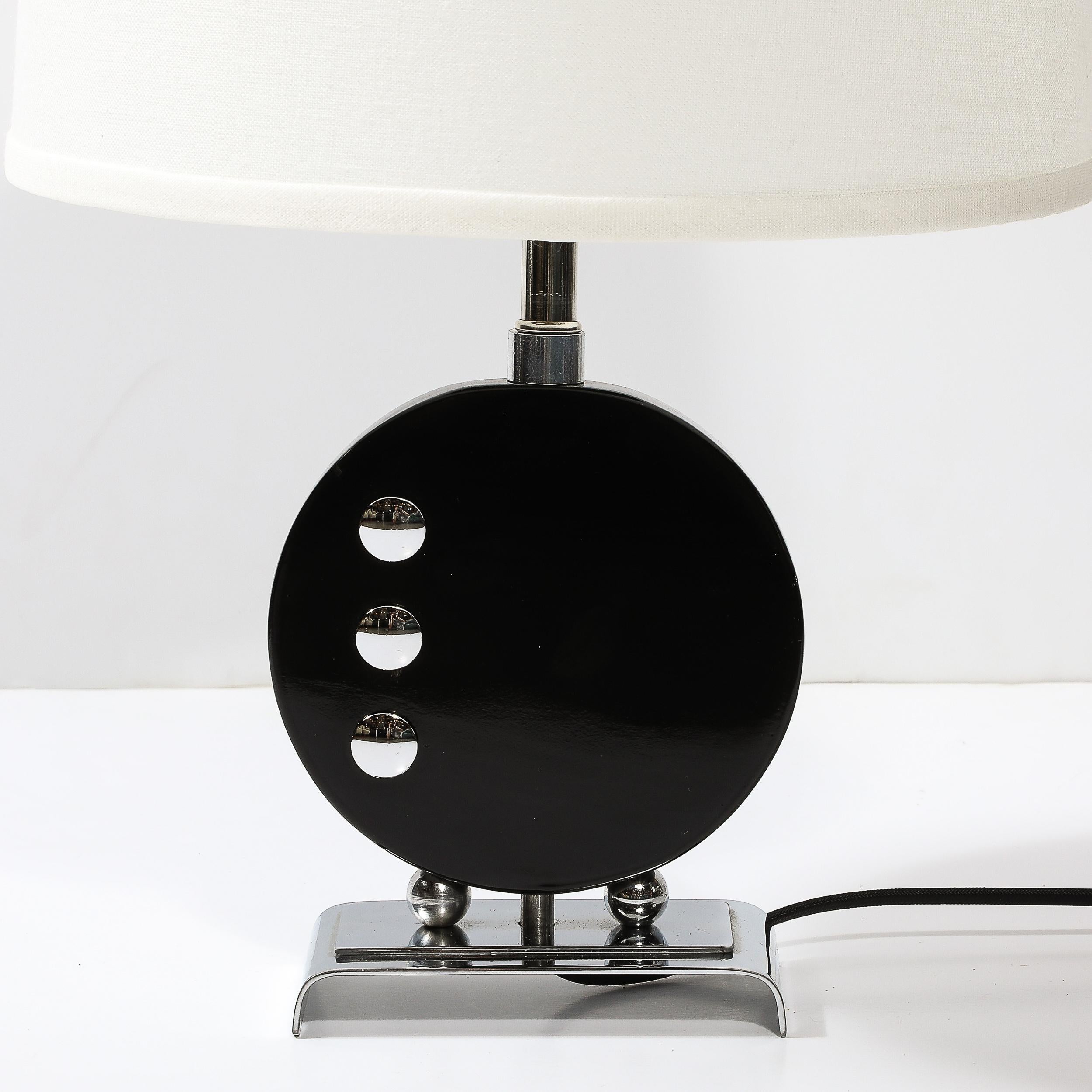Cette lampe de table Art déco en laque noire avec détails chromés d'après Donald Deskey provient des États-Unis, vers 1935. Le corps de la lampe est circulaire et laqué noir brillant. Trois accents chromés circulaires convexes se trouvent sur la