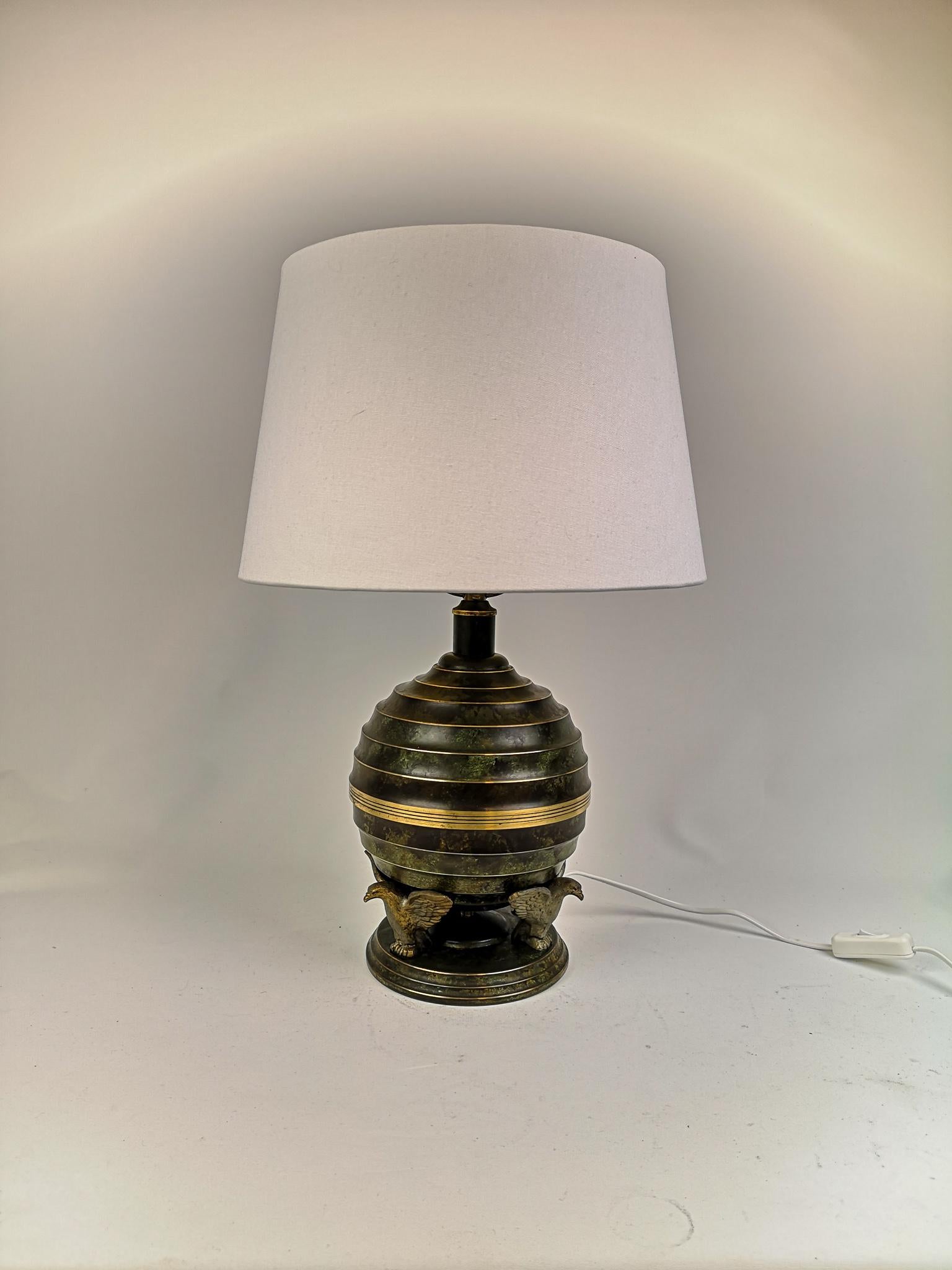 Wonderful table lamp made in Sweden. The lamp itself is made by SVM. It’s in patinated bronze and brass. The Art Deco round base is carried by three eagles.

It’s in good and working condition. Rewired. This is not the original shade.