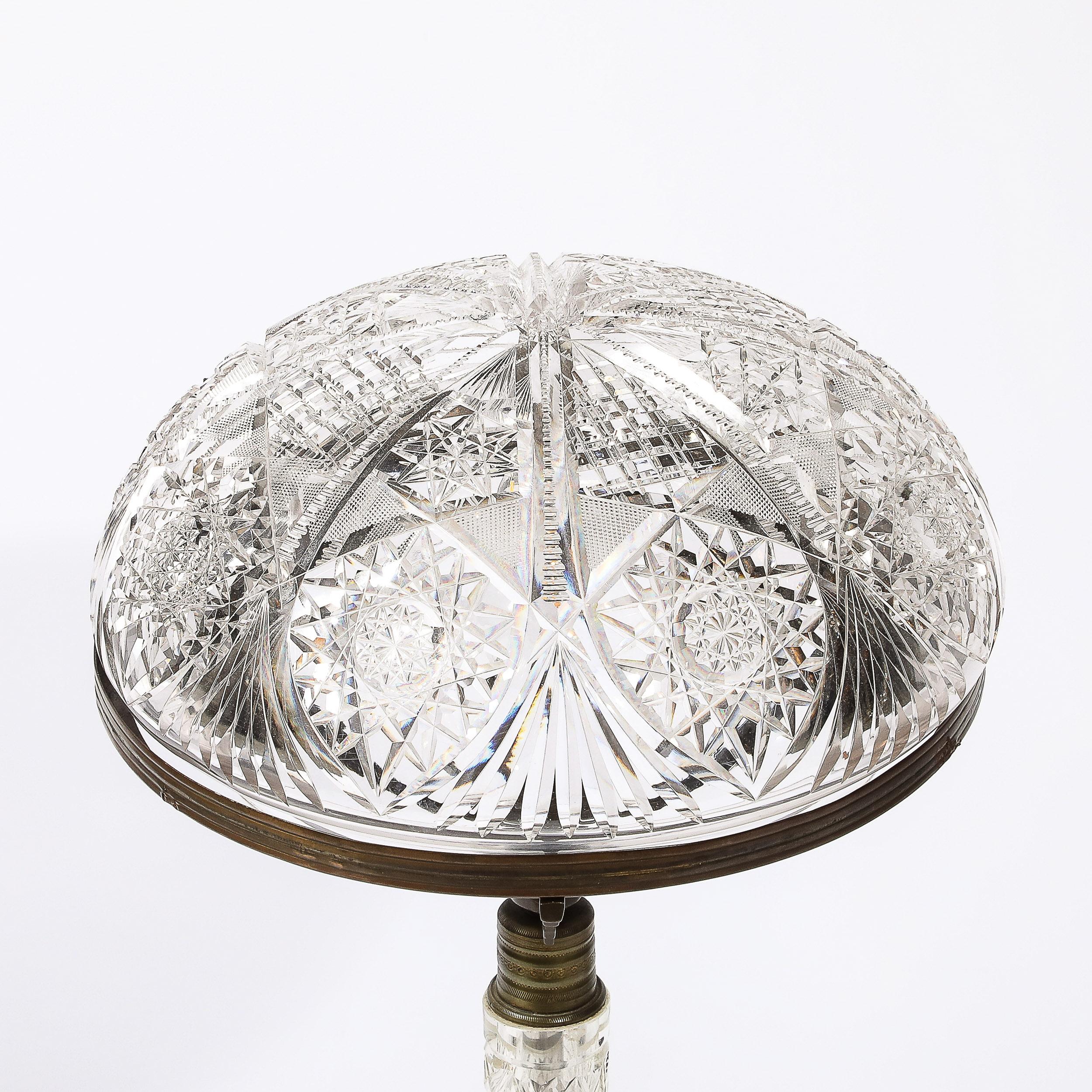 Diese glänzende Art Deco Tischlampe aus geschliffenem Kristall und Bronze stammt aus den Vereinigten Staaten, CIRCA 1925. Der kuppelförmige, geschliffene Kristallschirm mit stilisierten geometrischen Motiven und eleganten Details wird von drei