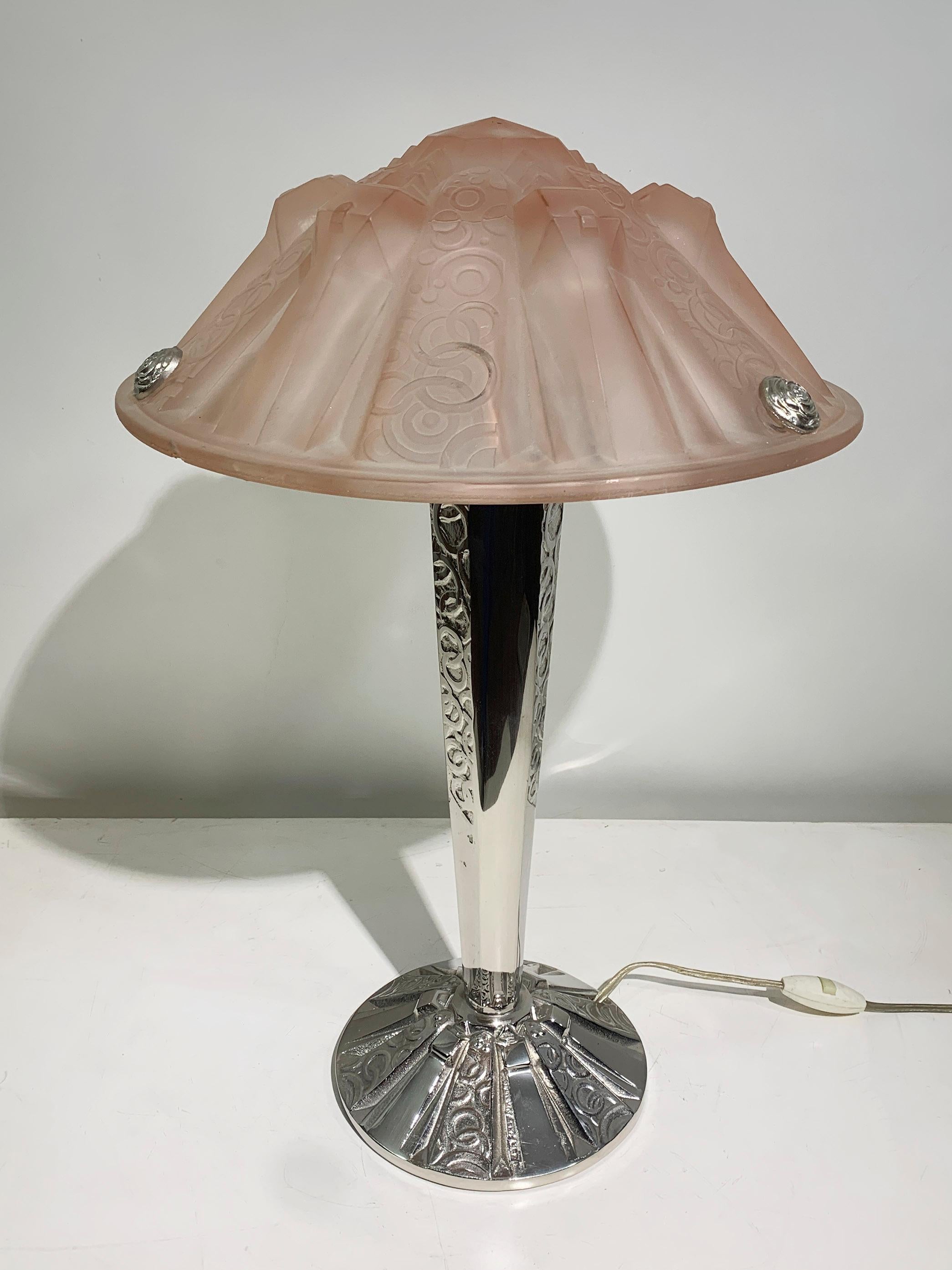 Cette exquise lampe de table Art déco, fabriquée par les célèbres verriers français Muller Frères, incarne l'élégance et la sophistication des années 1920. L'abat-jour en verre rose moulé sous pression est orné de bulles et de cercles complexes,