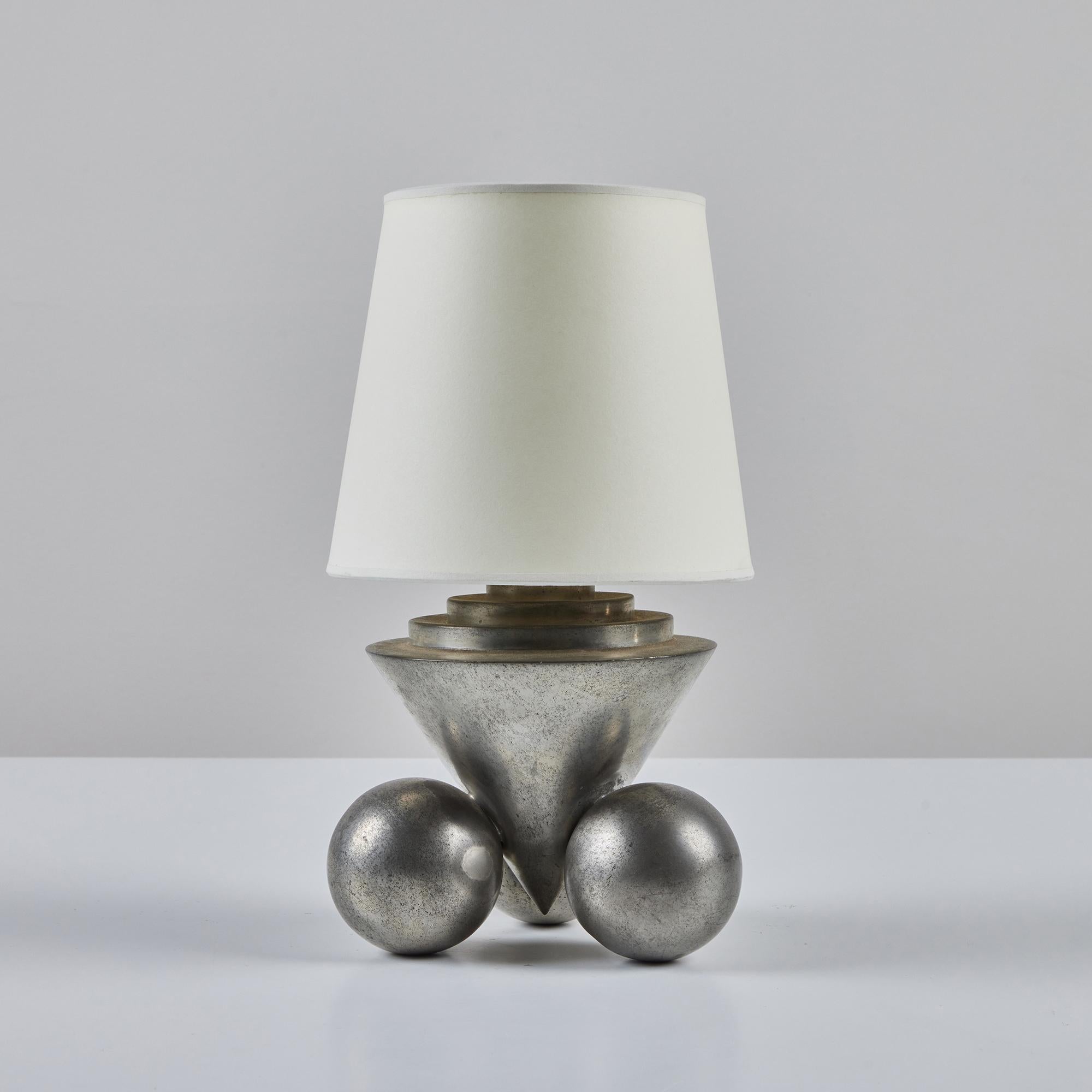 Petite Art Deco aluminum table lamp in the style of Chase USA. This lamp features an aluminum body with a cone center and three sphere feet. The lamp is finished with a new paper shade. The lamp has an on/off switch on the cord with two light