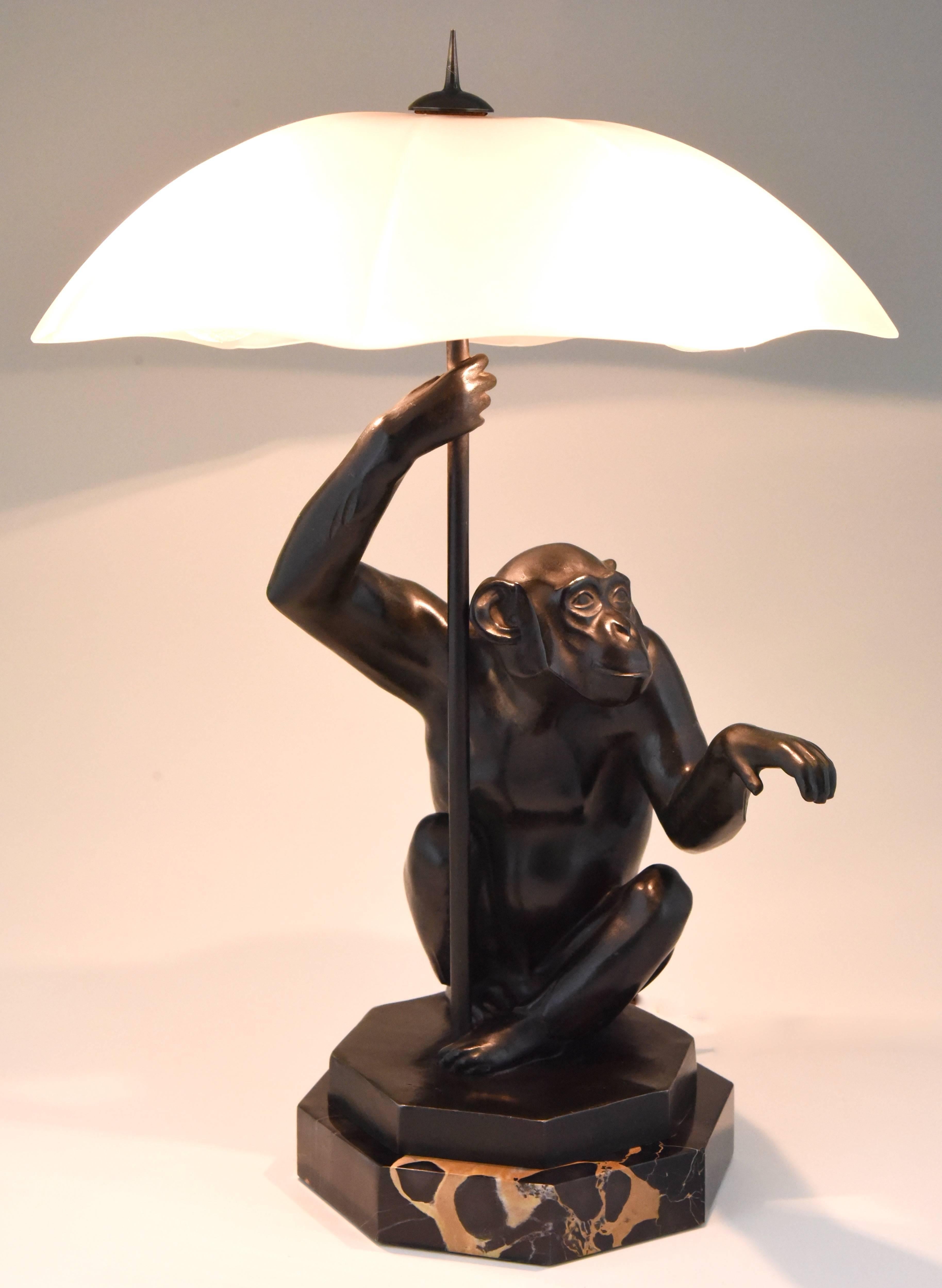 Description : Lampe de table Art Déco singe assis avec parapluie. 
Artiste / fabricant : Max Le Verrier. 
Signature / marques : Le Verrier. 
Le style : Art déco. 
Date : 1930. 
Matériau : Métal patiné vert. Base en marbre Portor. Abat-jour en verre