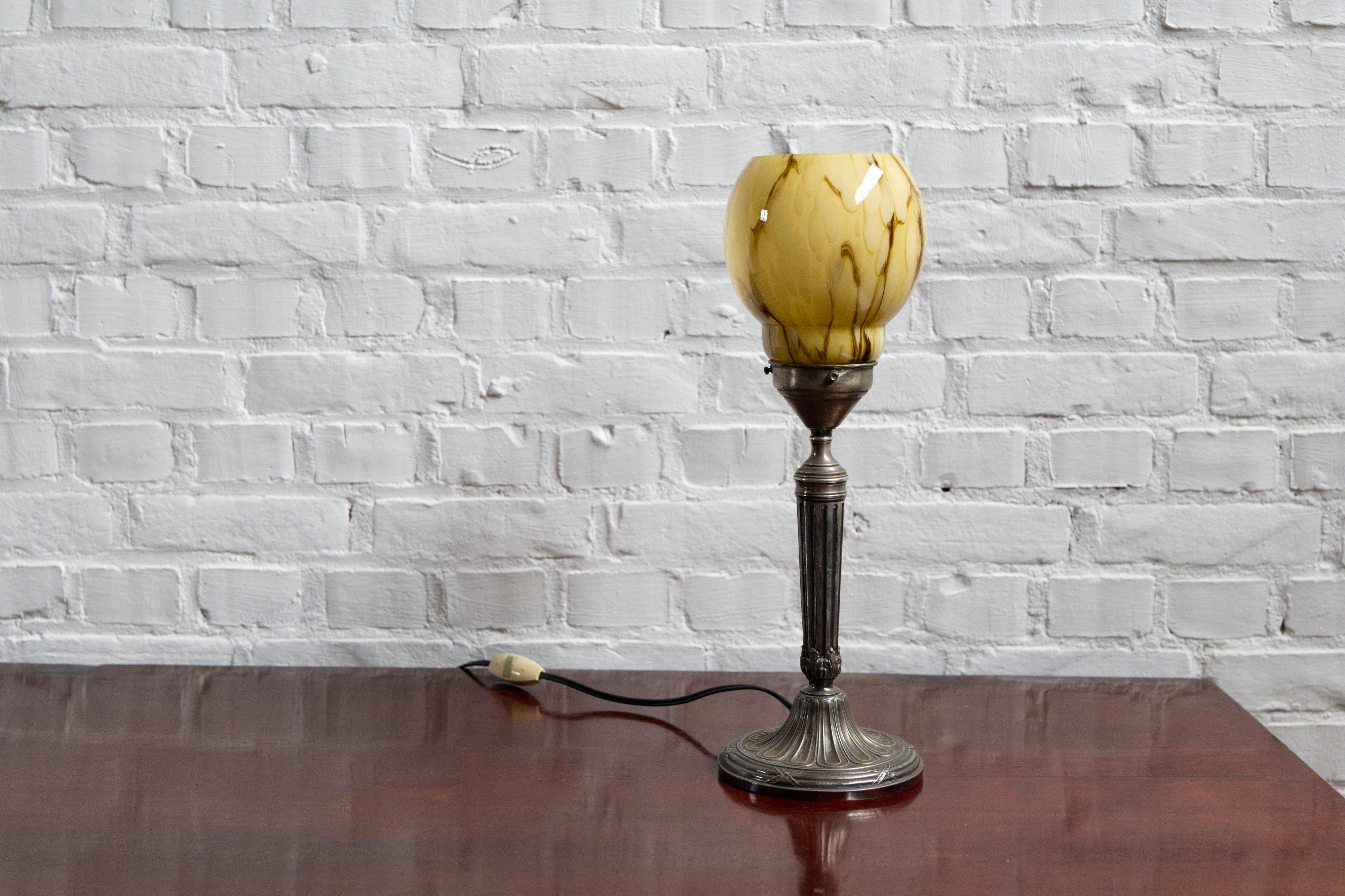 This Art Deco table lamp combines timeless elegance with intricate craftsmanship. The lamp features a detailed relief design engraved into its base, showcasing a sophisticated, geometric pattern that reflects the opulence of the Art Deco era.

The