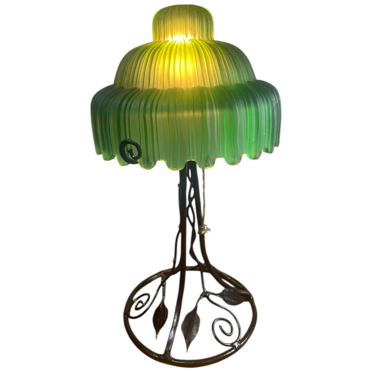 Lampe de table, abat-jour en verre vert, base en fer forgé avec motif de vigne.
L'abat-jour présente quelques rayures.