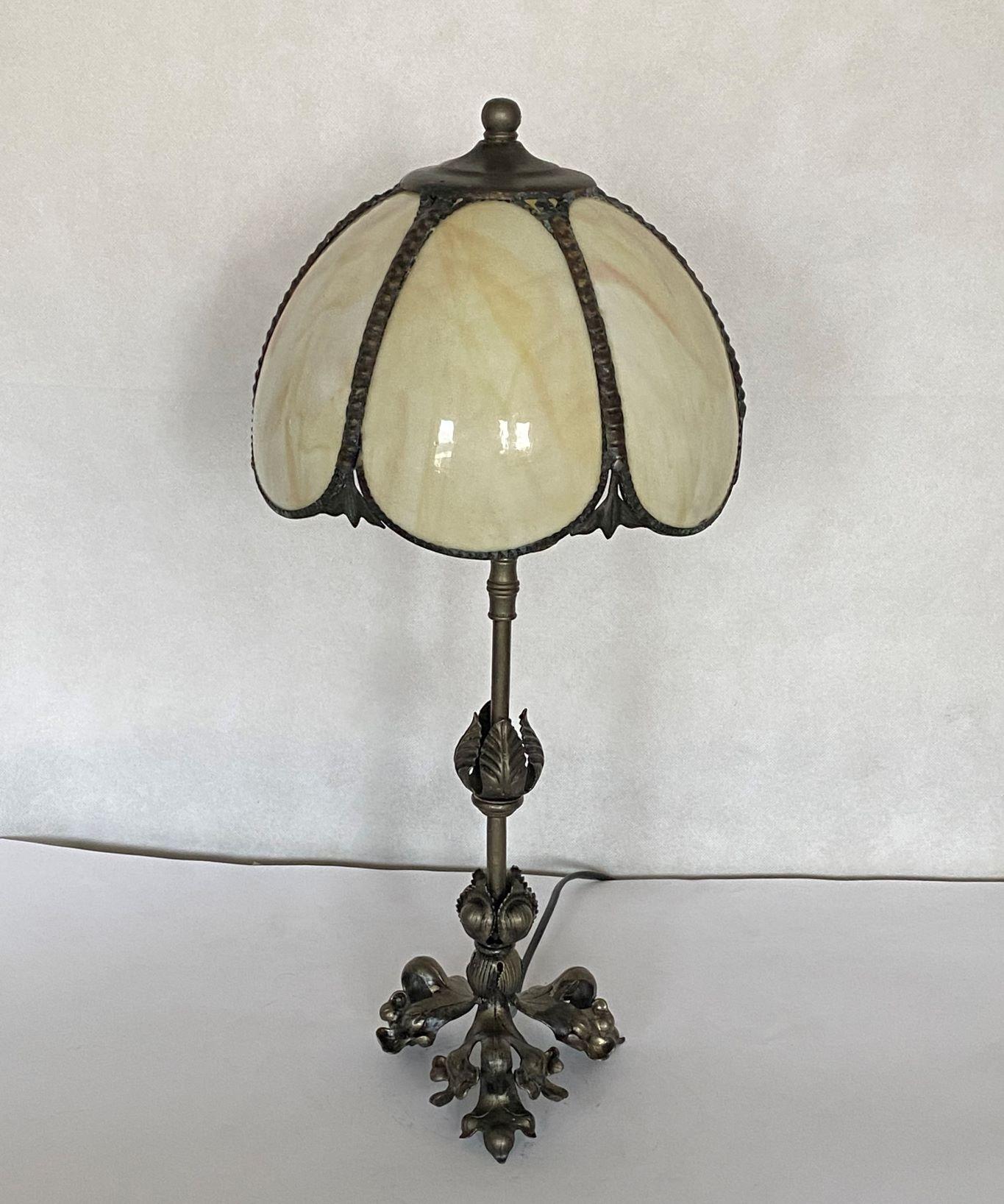A tall, elegant French Art Deco table lamp from the 1930s. Dome form shade with six bent slag glass panels beautifuly connected with brass, providing a warm, pleasant lighting, on a foliate tripod patinated wrought base. The table lamp is in fine