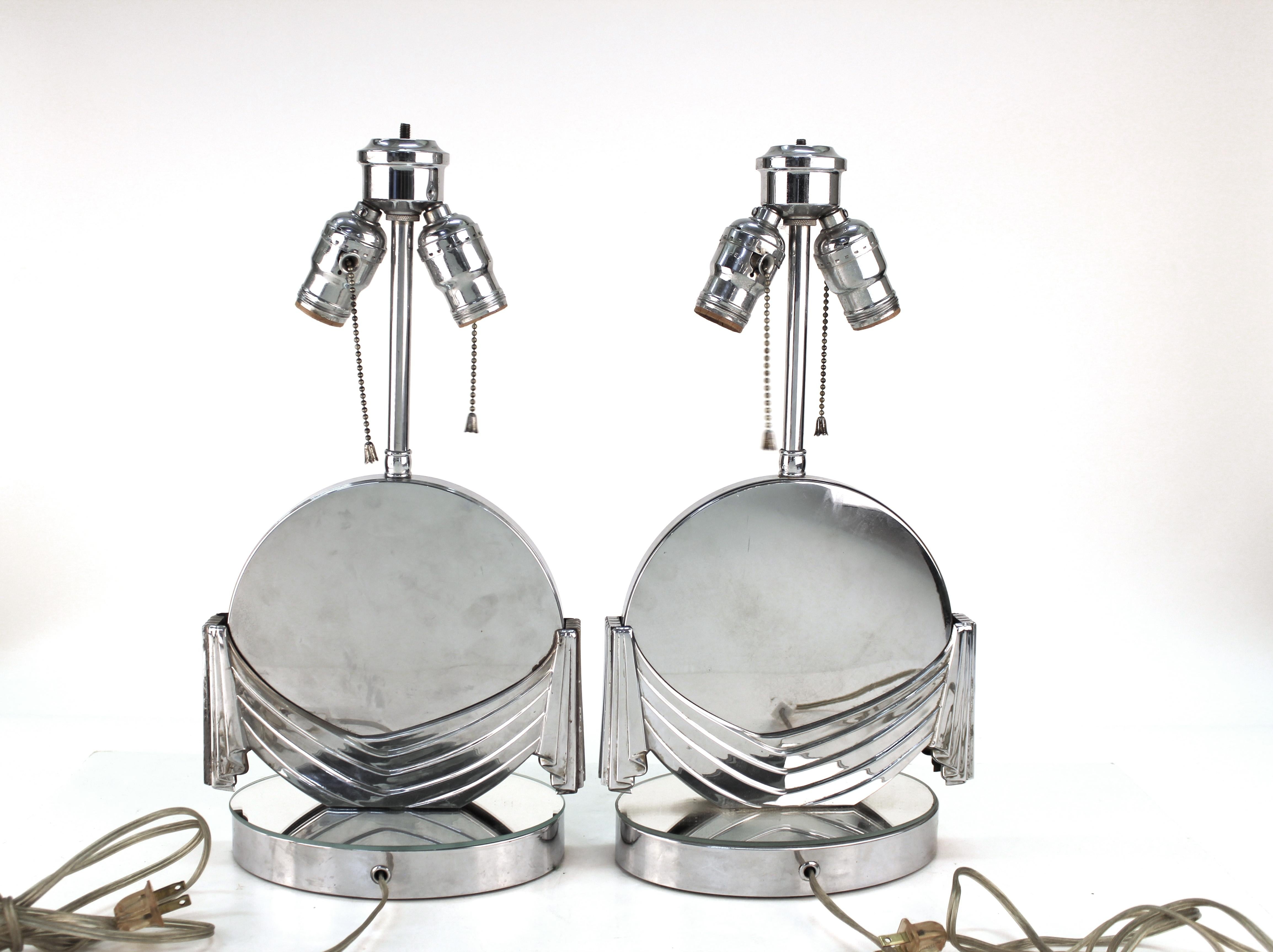 Art Deco table lamps with silver tone mirrored finish. The lamps Stand on circular bases and feature round bodies partially hidden behind stylized 'drapes.' Some wear includes patina, spotting to the metal and surface scratches appropriate to age