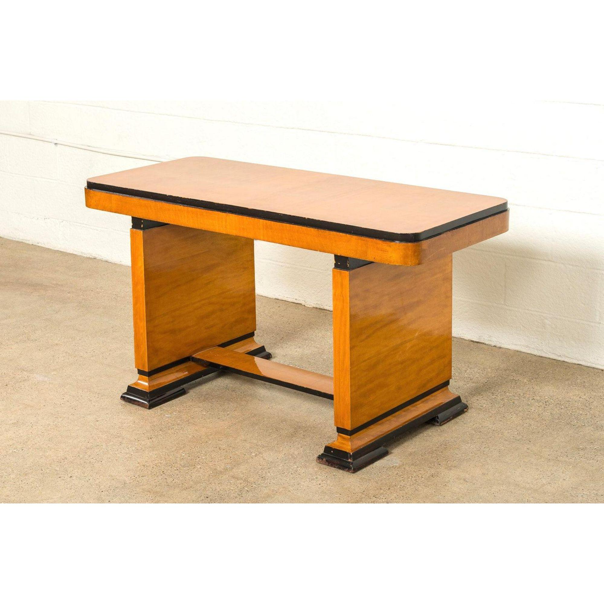 This lovely Art Deco table or writing desk circa 1930 is expertly handcrafted from maple wood and features a rectangular tabletop with curved edges and tall apron, a trestle base and ebonized accents.