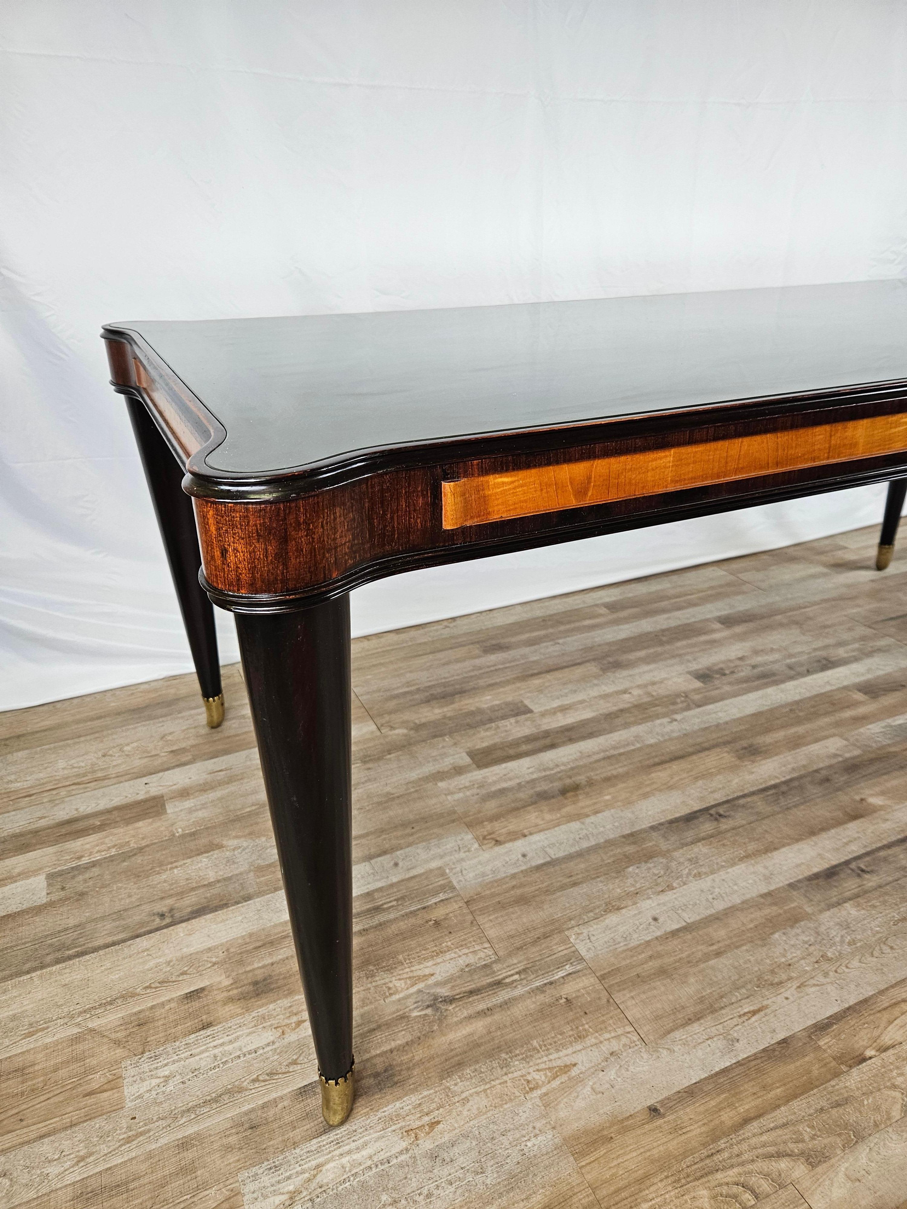Elegant Italian-made dining table with teal glass top and structure in various types of wood.

It is a design piece of furniture, a 1950s piece of furniture with ebony legs and mahogany structure with central details in pink maple.
Note the