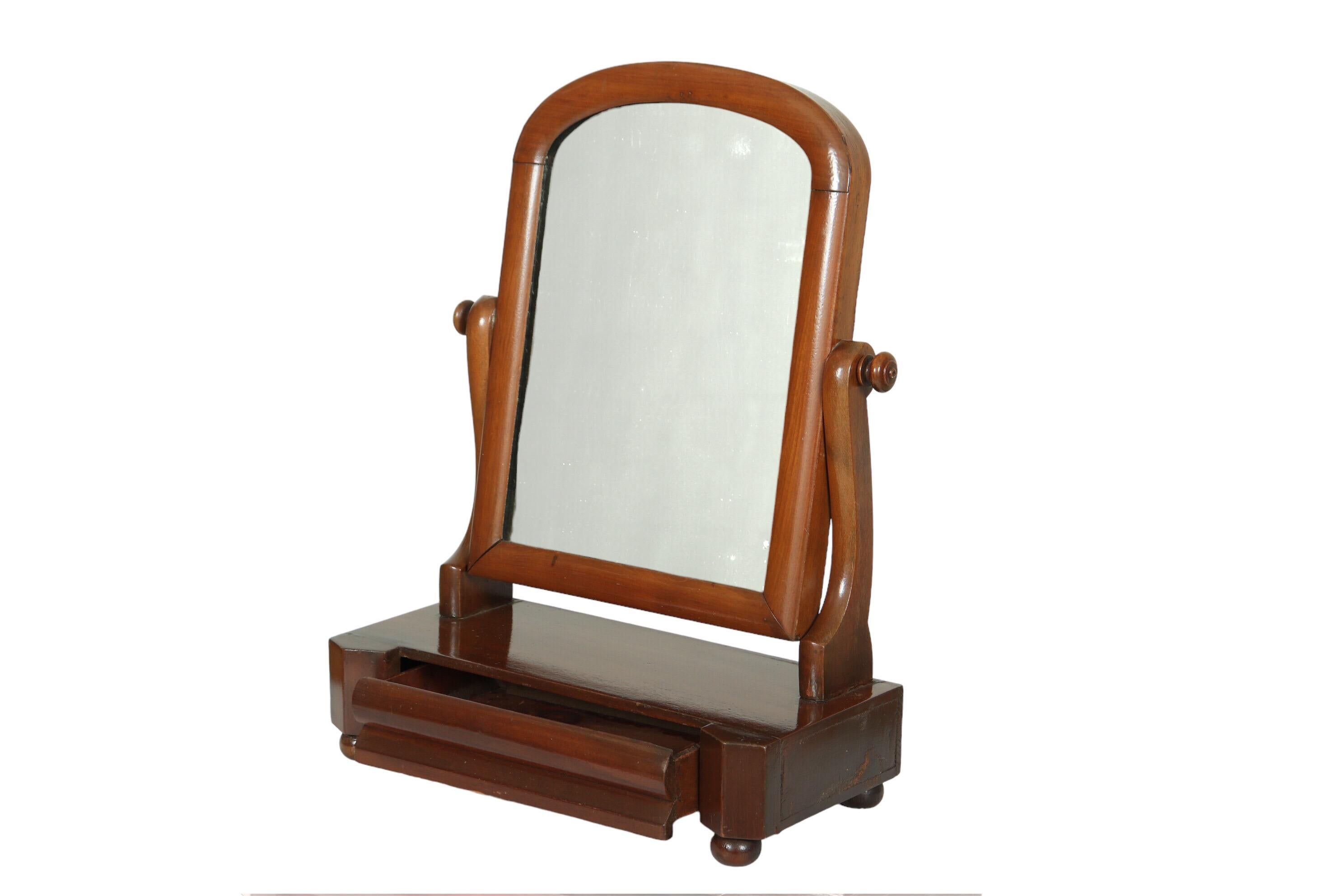 An Art Deco tabletop vanity mirror with a single drawer. An arch shaped mirror on curved supports can be tilted forward and back. A dovetailed drawer below, has a beveled front and sits between angular posts above bun feet.