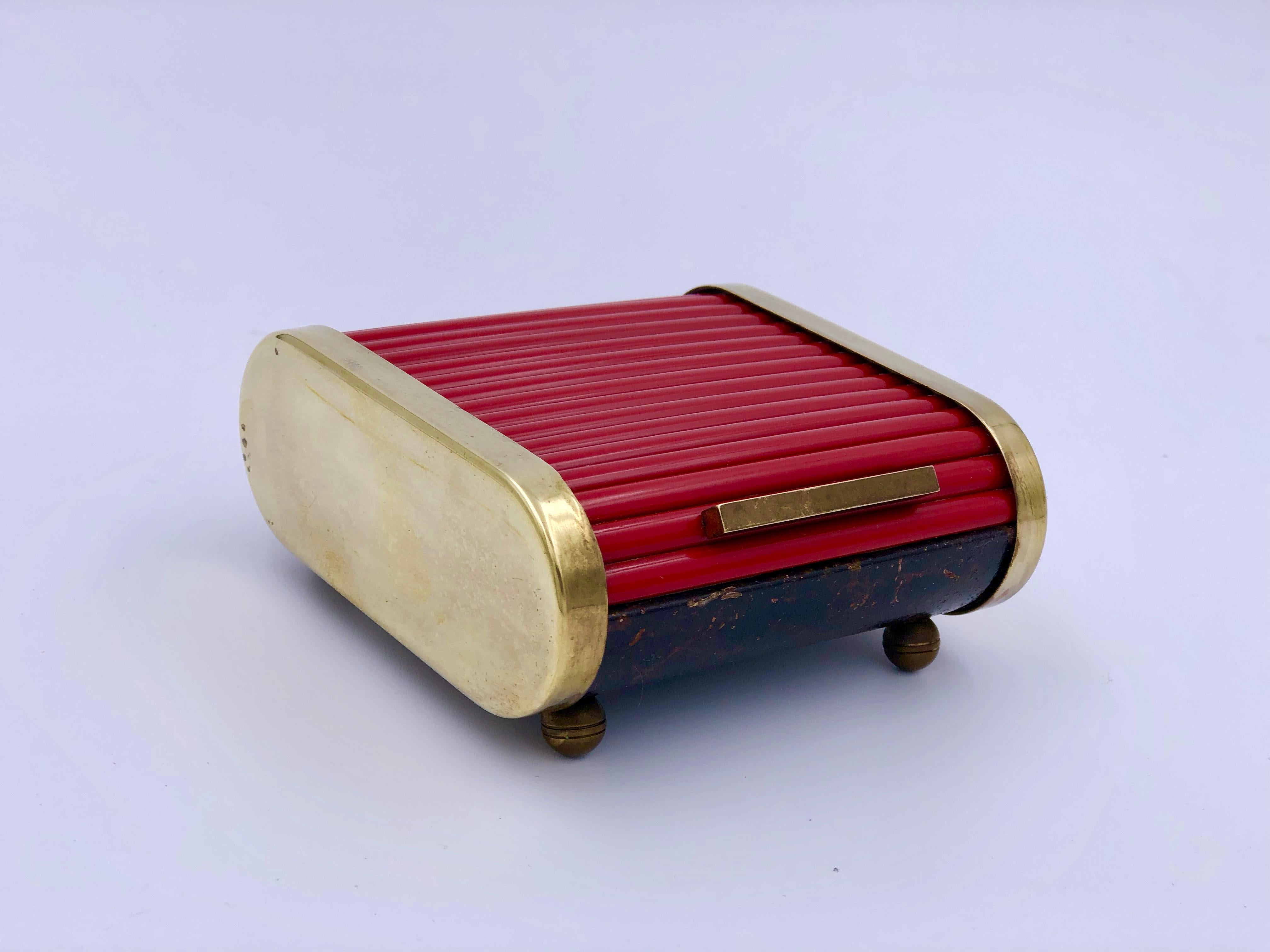 Early 20th century American Art Deco industrial desk storage caddy or cigarette holder by Park Sherman. The box has a tambour style top made of red bakelite and a faux marble base. It has brass accents on either side, a brass handle, and is raised