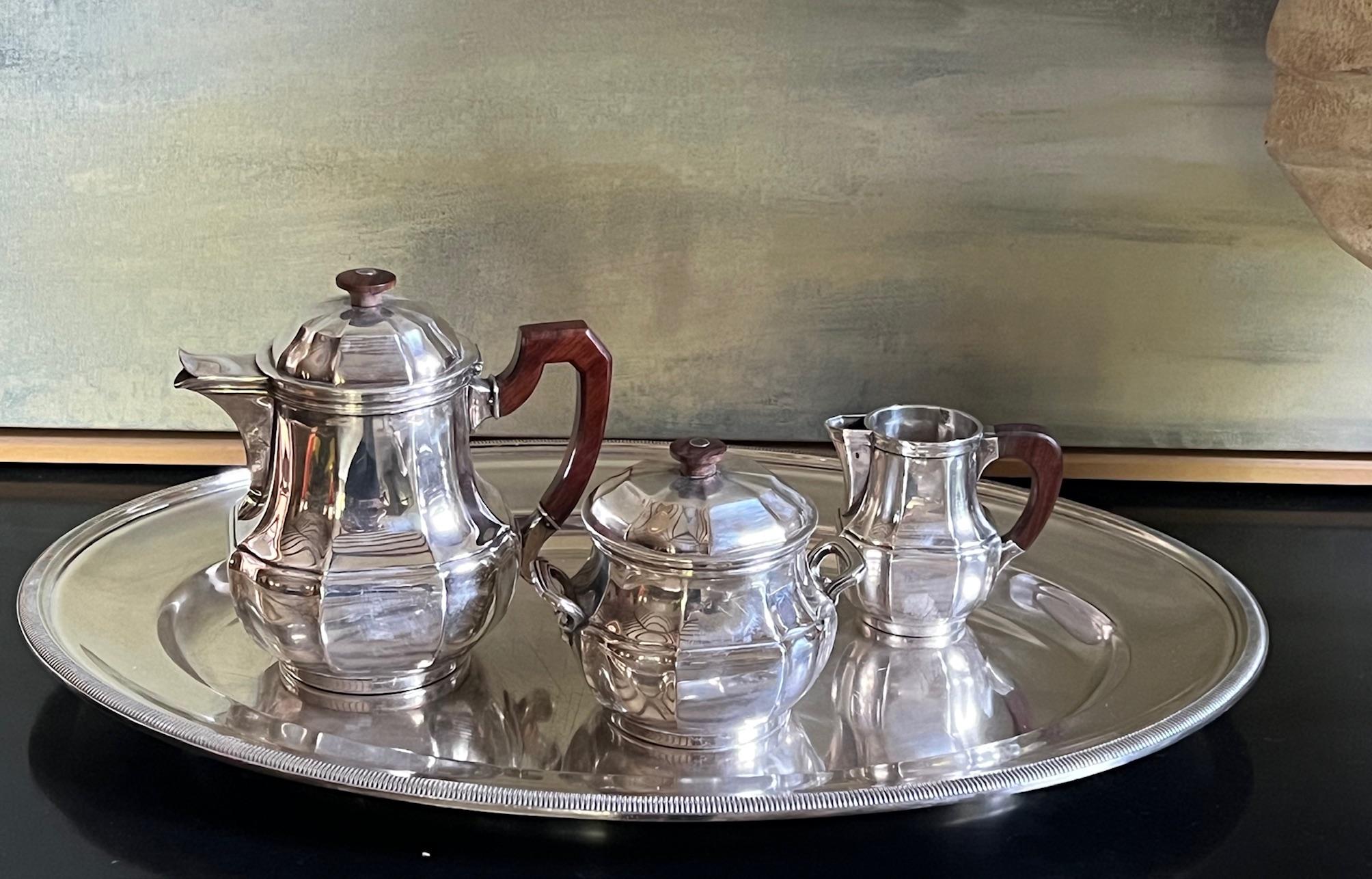 Service à thé de style Art déco fabriqué par Christofle en France dans les années 1930. L'ensemble comprend un grand plateau ovale, une théière, un sucrier à couvercle et un crémier. Deux des pièces ont des poignées en bois de rose. 

Théière : 7.1