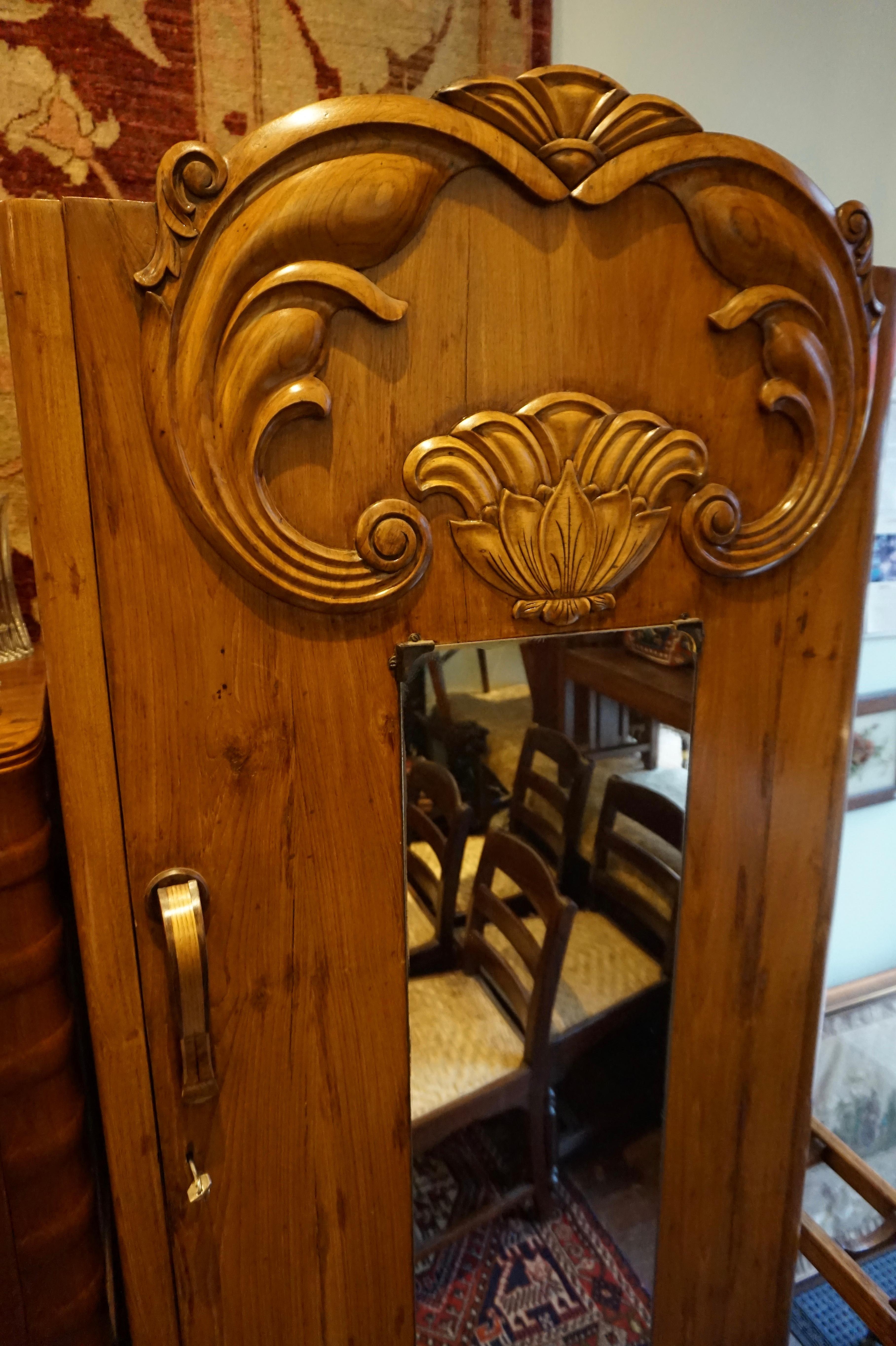 Art Deco Armoire constructed from solid teak with a hand carved facade and steamed edges. Beautiful flowing golden grains of teak wood. Single piano hinge supporting solid door frame. Inside it houses two drawers and a hanging rack. Raised on a