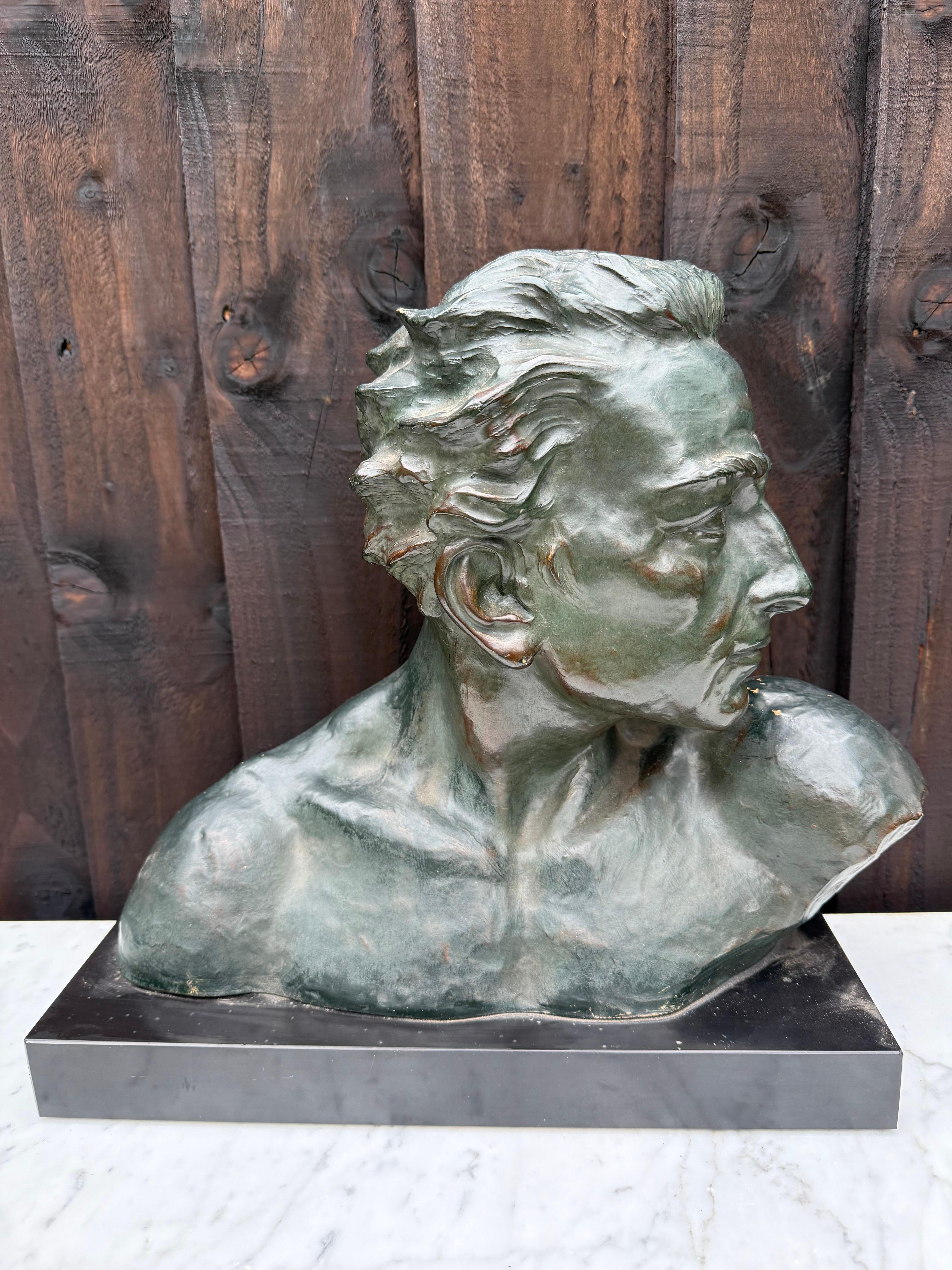 Beautifully expressive statue from the Art Deco period, bust of a young man, 'En Profil' The statue is made of terracotta with a black marble base. The statue is patinated in a green with bronze color. On the back is the signature of the artist,
