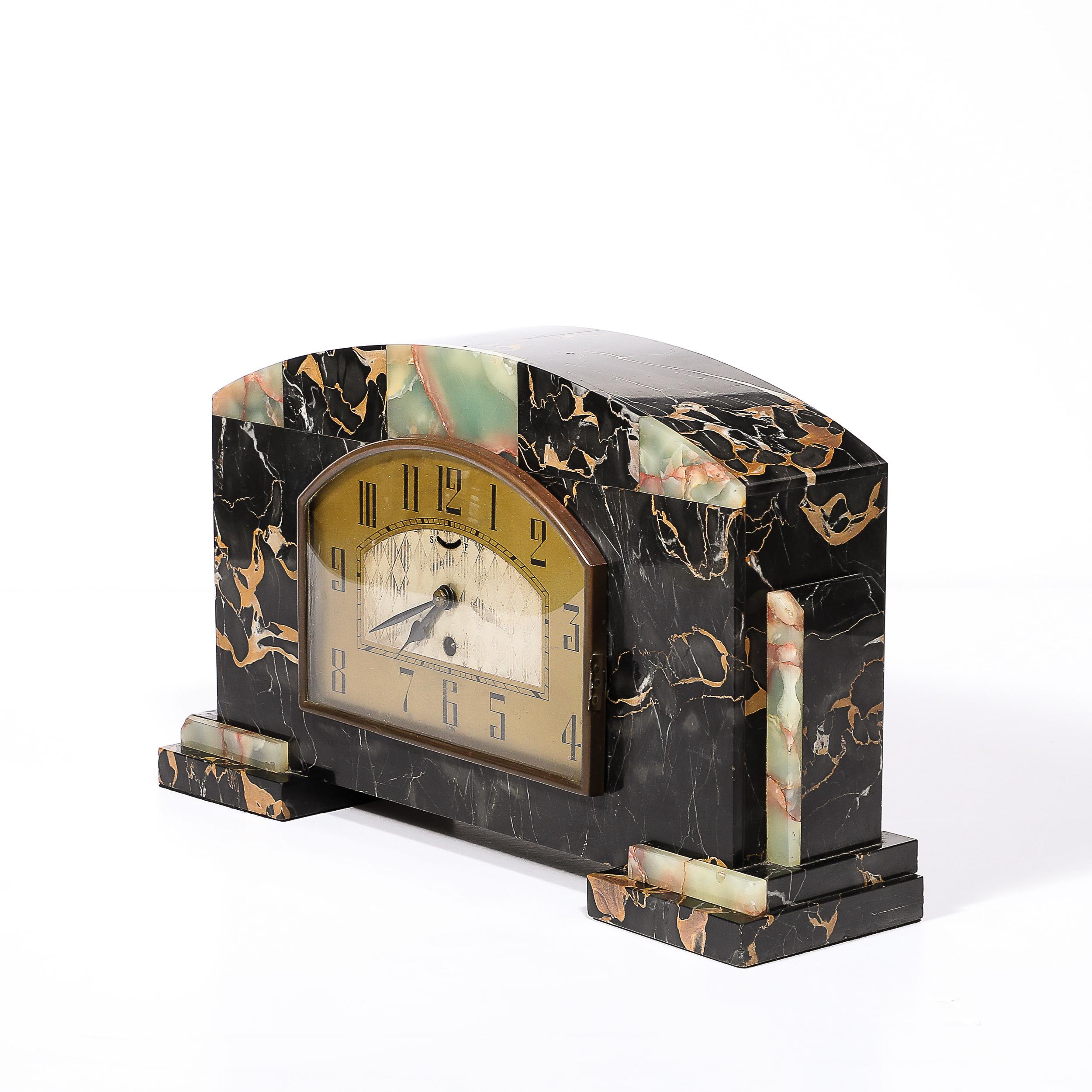 This impactful and elegant Art Deco Tessellated Marble,onyx  & Brass Mantlepiece Clock signed Ucra originates from France, Circa 1935. Featuring an arched composition in two varieties of variegated marble with a two part tiered plinth base on either