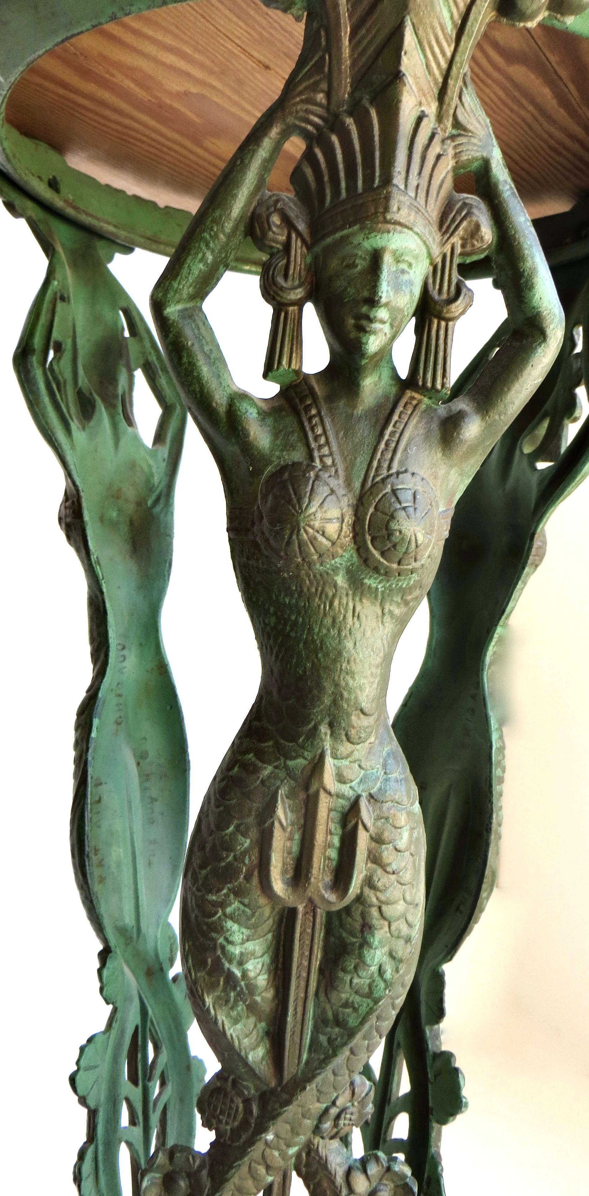 In questo caso si tratta di un tavolo figurato Art Deco in stile classico Revival egiziano molto dettagliato, con tre bellissime sirene in ghisa in piena regalità con copricapi e abiti tipo Regina Nefrodite, con gambe e piedi che terminano con code