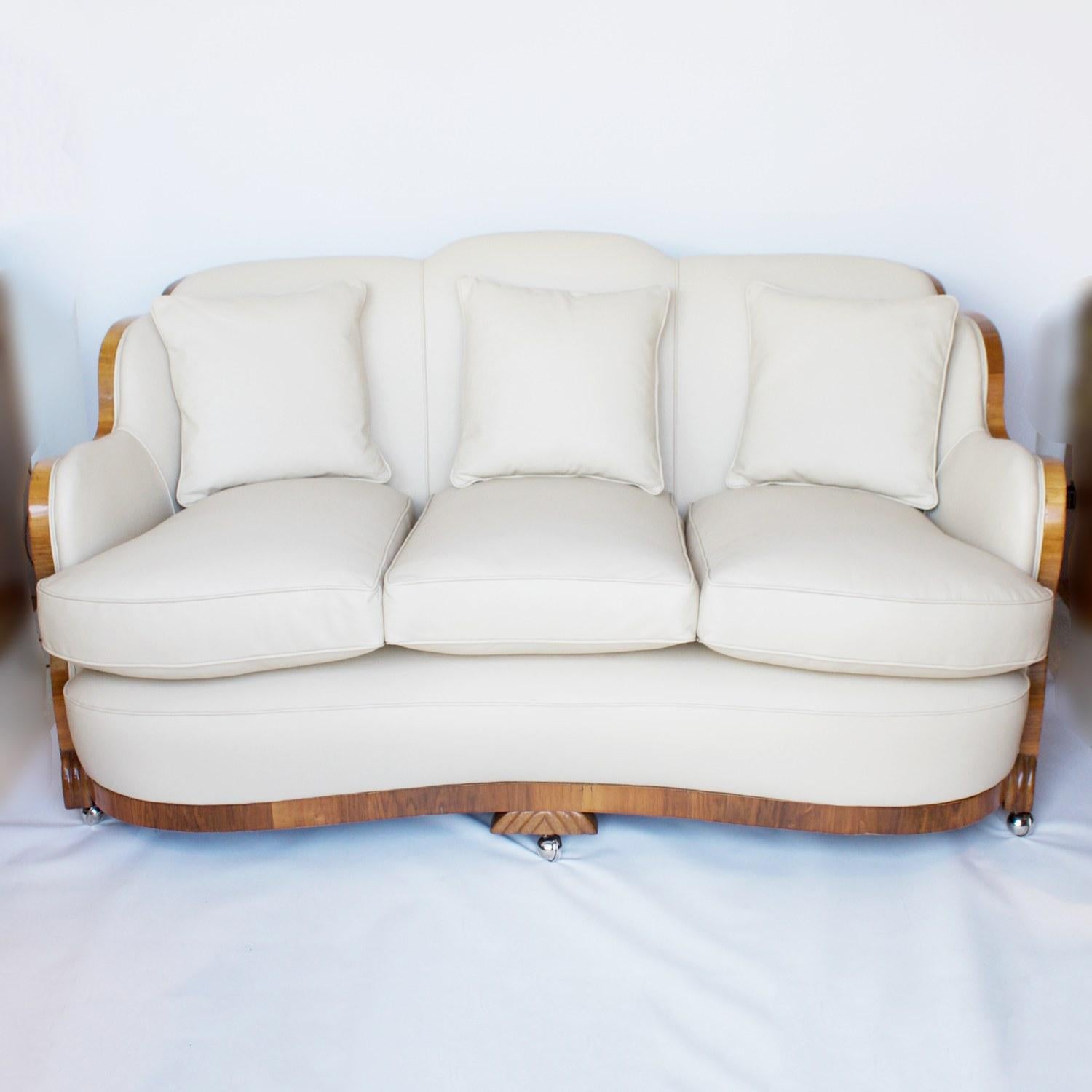 An Art Deco three-piece suite by Harry & Lou Epstein comprising of a three-seat sofa and two lounge chairs. Burr Walnut veneered wrap around veneers with a straight grain walnut banding. Fluted carved swirl detail to sides of feet and centre of