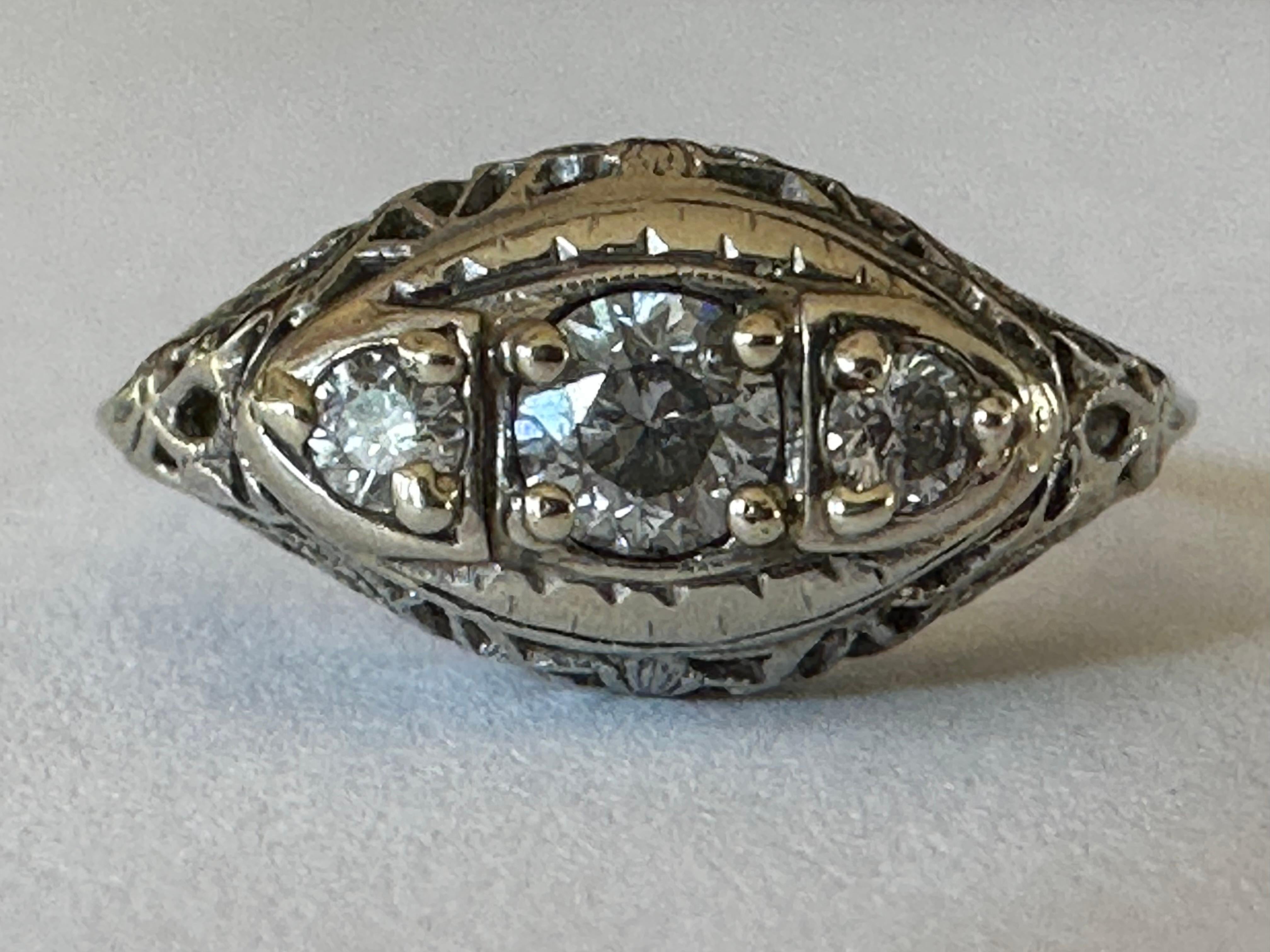 Three Old European cut diamonds line the top of this Art Deco band complemented with fine filigree and set in 10K white gold. The center diamond totals approximately 0.20 carats and is flanked by two smaller diamonds each totaling approximately 0.05