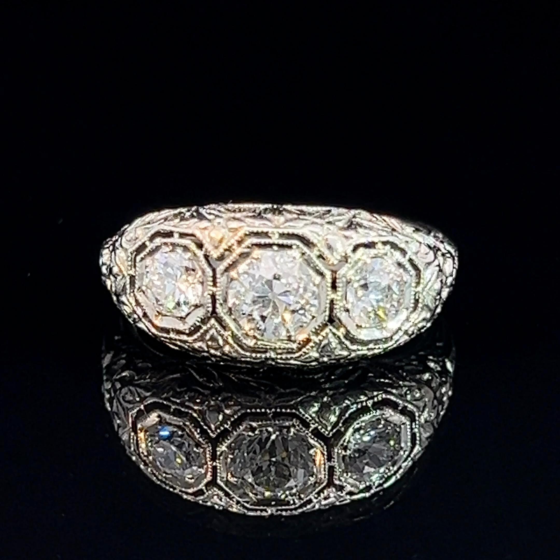 Art Deco white gold wide three-stone diamond ring featuring pierced filigree setting with hand engraved floral motifs.

Diamond: One 4.8mm early European cut diamond H-J colour, I1 material, estimated weight 0.50ct
Diamonds: Two 3.75mm early