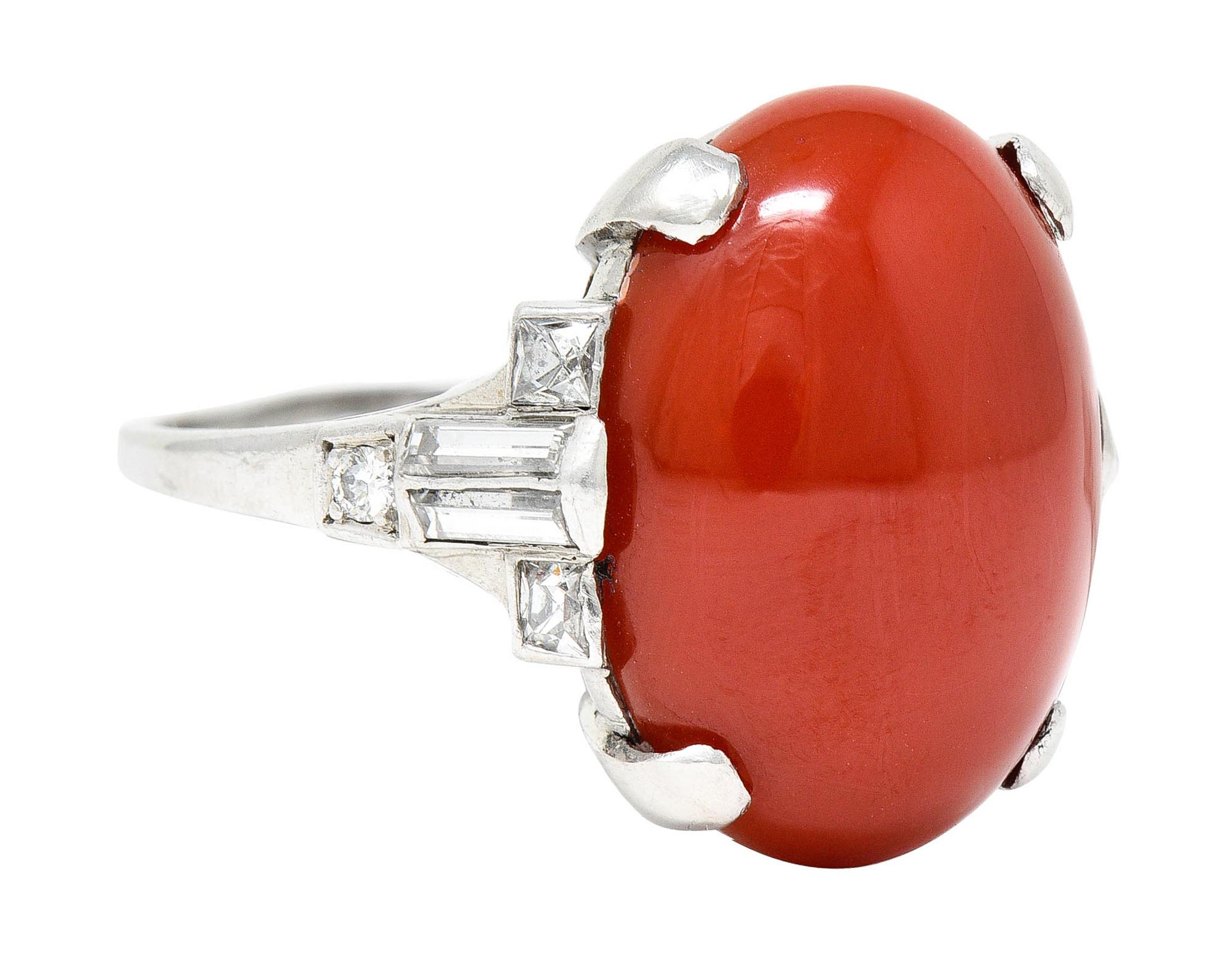 Centering an oval cabochon of coral measuring approximately 19.0 x 14.5 mm

Opaque with slightly orange and vibrantly red color - uniform in distribution

Basket set by wide prongs and flanked by geometric shoulders

Set with baguette, French, and