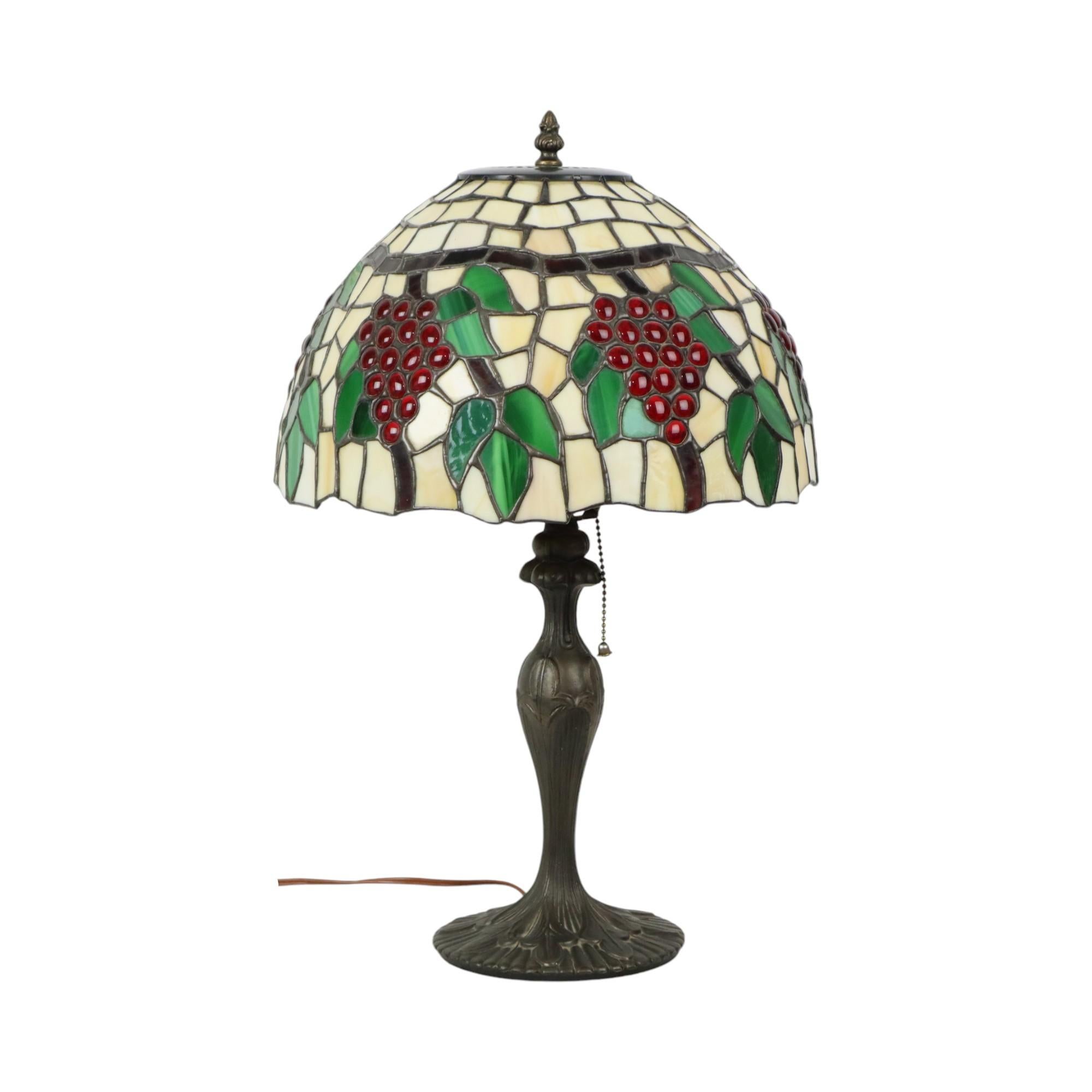 Beautiful Tiffany style table lamp, lamp with stained glass lampshade, image of bunches of grapes and leaves, inspired by the art deco movement, with an organic art nouveau style base, circa 1970s. Still has its original wiring, plug and pull cord,