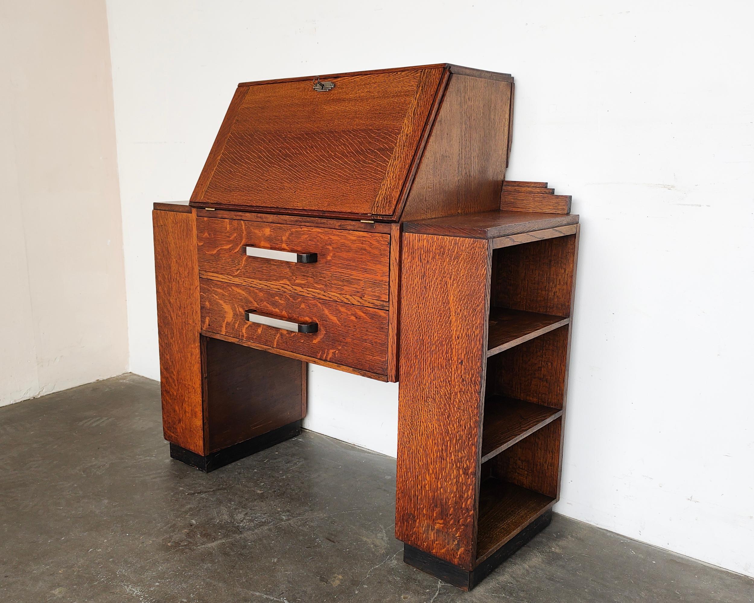 Beautiful Art Deco bureau bookcase / secretary desk. Solid tiger oak construction featuring open bookshelves on each side. Two drawers in the center with original metal and contrasting wood pulls. Drop-down cabinet door opens to writing surface,