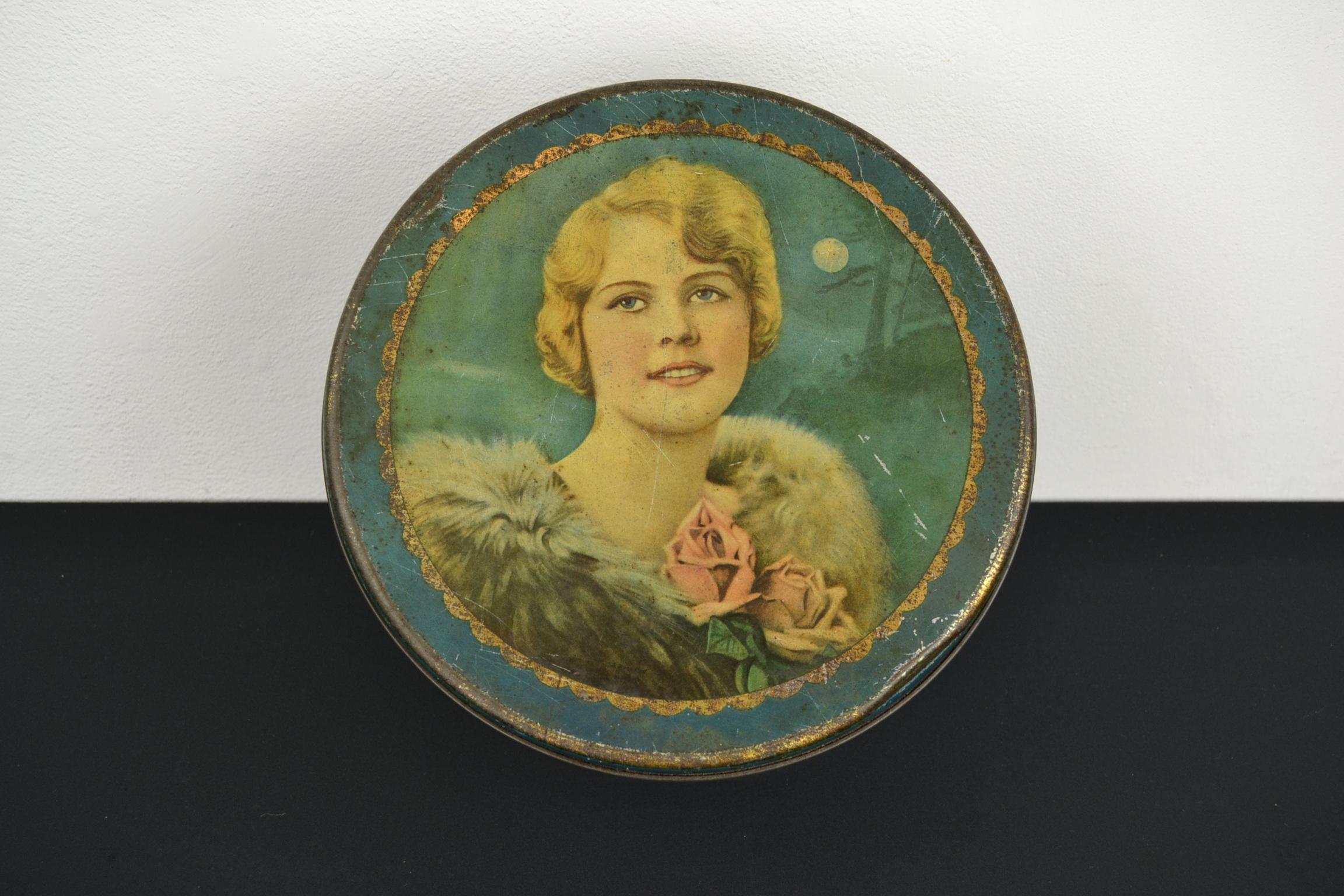 Art deco tin with a woman with stola around her neck.
This elegant lady has blond eyes and blue eyes. 
This round lithographic antique biscuit tin dates circa 1930s. 
Made by Ets. J. Schuybroek - Hoboken - Anvers - Antwerp- Belgium.
It's a blue