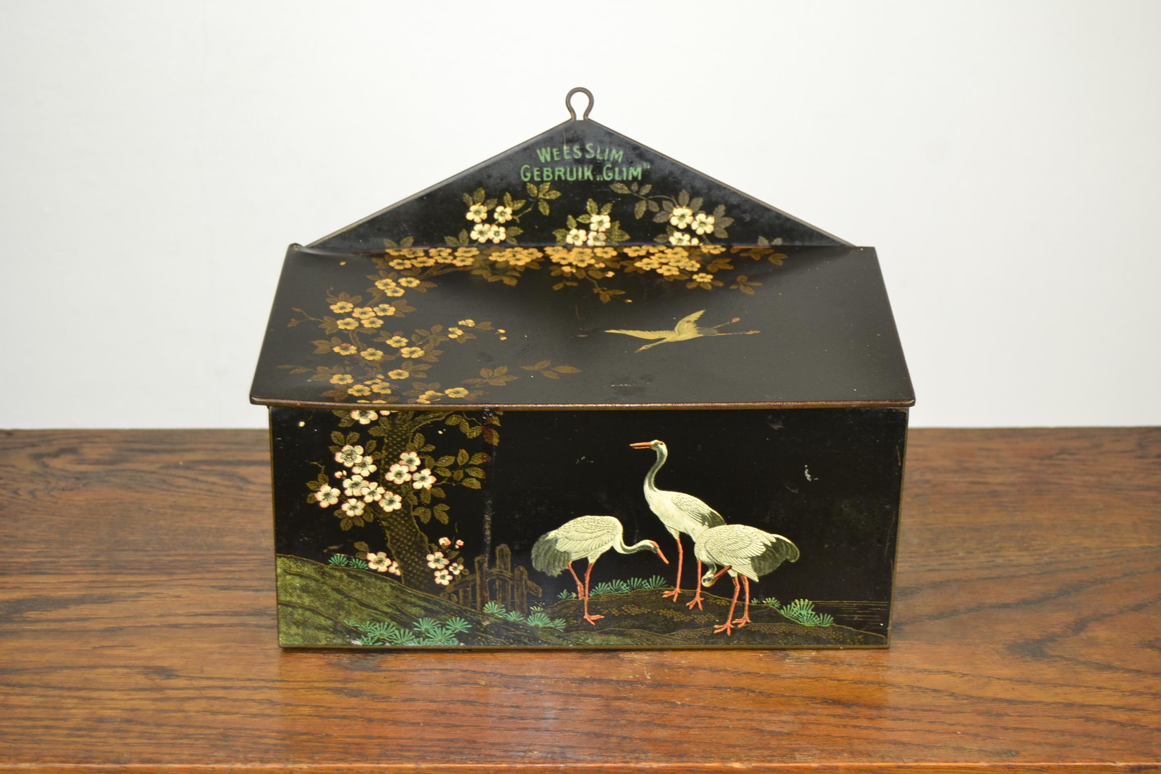 Black Art Deco tin with crane birds and flowers in Asian style.
This Art Deco storage tin with cranes dates from the early 1930s and was made by the Dutch Company Bekkers Dordrecht Holland. 
It was designed to storage cleaning and polishing