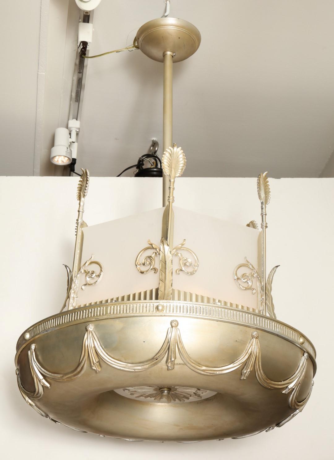 A pair of antiqued silver-leaf Art Deco chandeliers with a torus shaped frame and swag motifs. American, circa 1930s. Chandeliers feature glass panels around the top and a cast starburst shaped element on the underside with a piece of round frosted