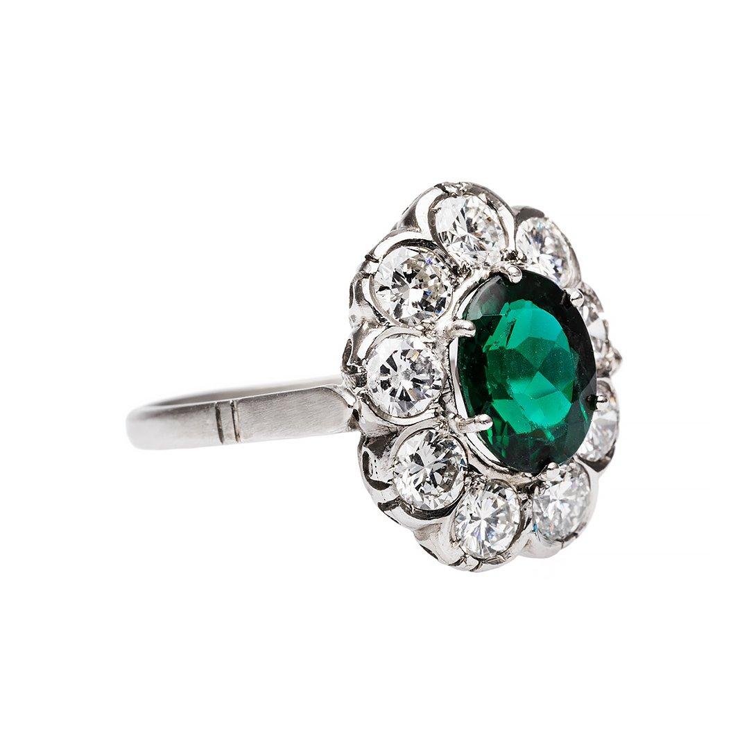 Art Deco is a style of visual arts combining architecture and design that first originated in France before the commencement of the first world war. Featuring a unique pine green tourmaline that has been crowned with a halo of old cut diamonds