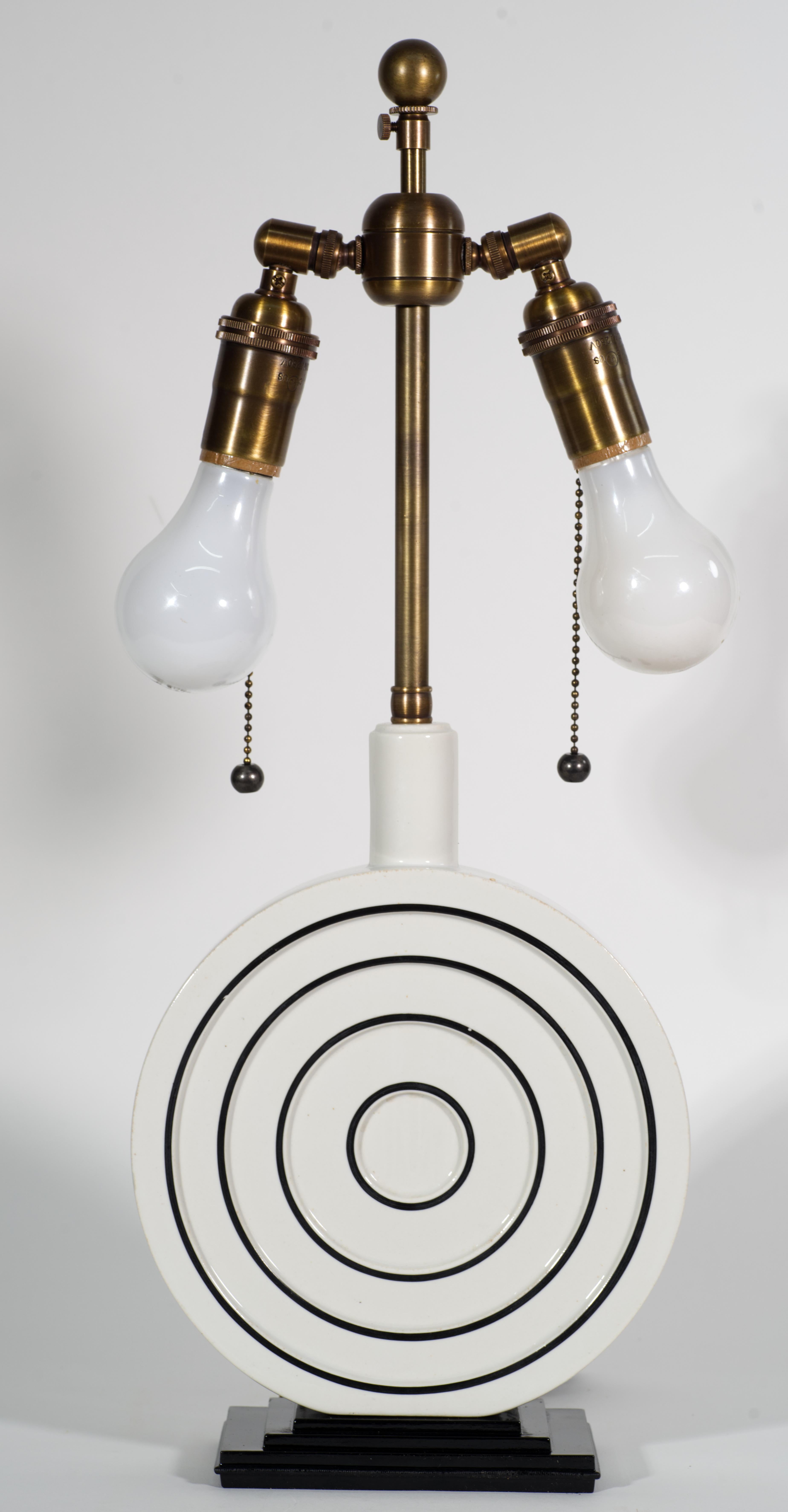  Rare, unusual table lamp features disc shaped ceramic base with circular graphic design delineated in black on molded relief on off-white background. The base is mounted on rectangular black metal base with characteristic Art Deco silhouette. The