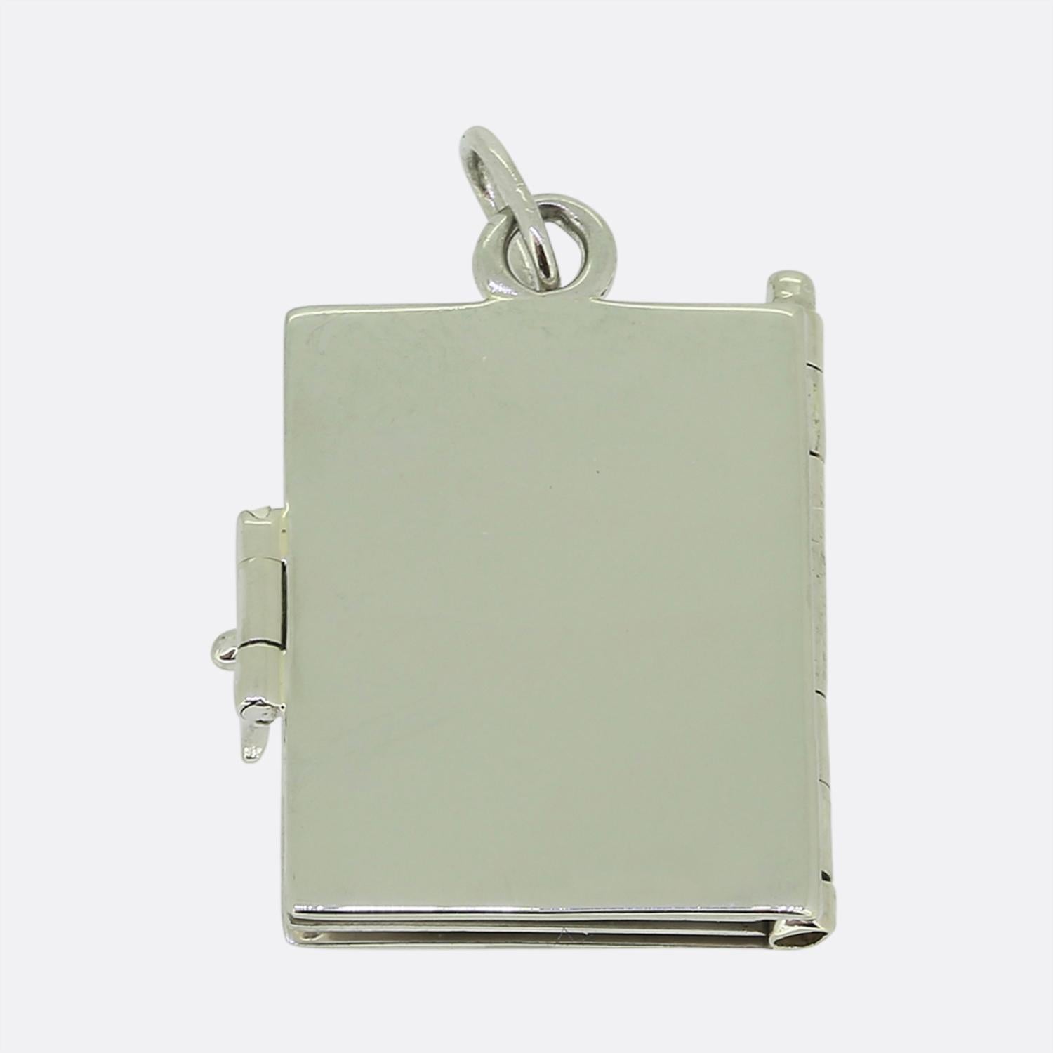 Nous avons ici une breloque raffinée en or blanc 18ct, façonnée en forme d'album. Le charme présente une surface élégante et polie avec deux diamants de taille trilobée sertis aux angles, ajoutant une touche de sophistication et d'éclat. La pièce