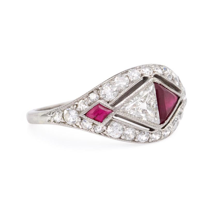 An Art Deco ring comprised of facing triangular-cut ruby and diamond and flanked by small opposed kite-shapes, in a round-cut diamond surround, in platinum.