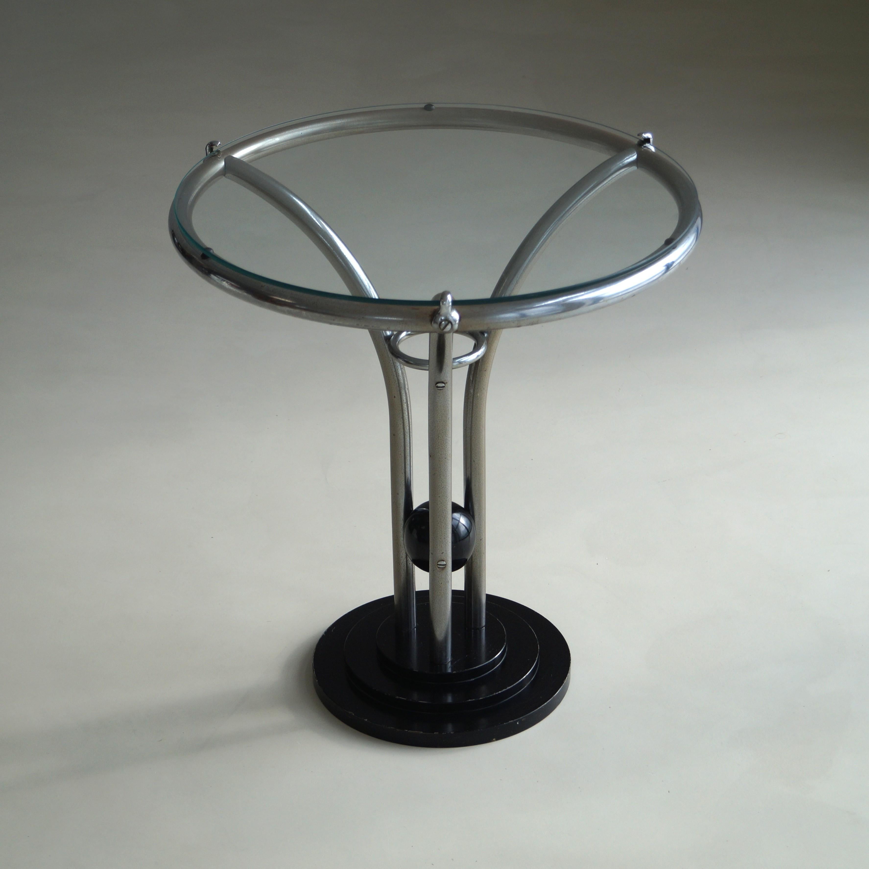 A striking example of 1930s Art Deco design, this side table captures the streamlined elegance of the Machine Age. Featuring a tubular chrome frame, circular glass top, and a sculptural black lacquered stepped base with a central sphere, the piece
