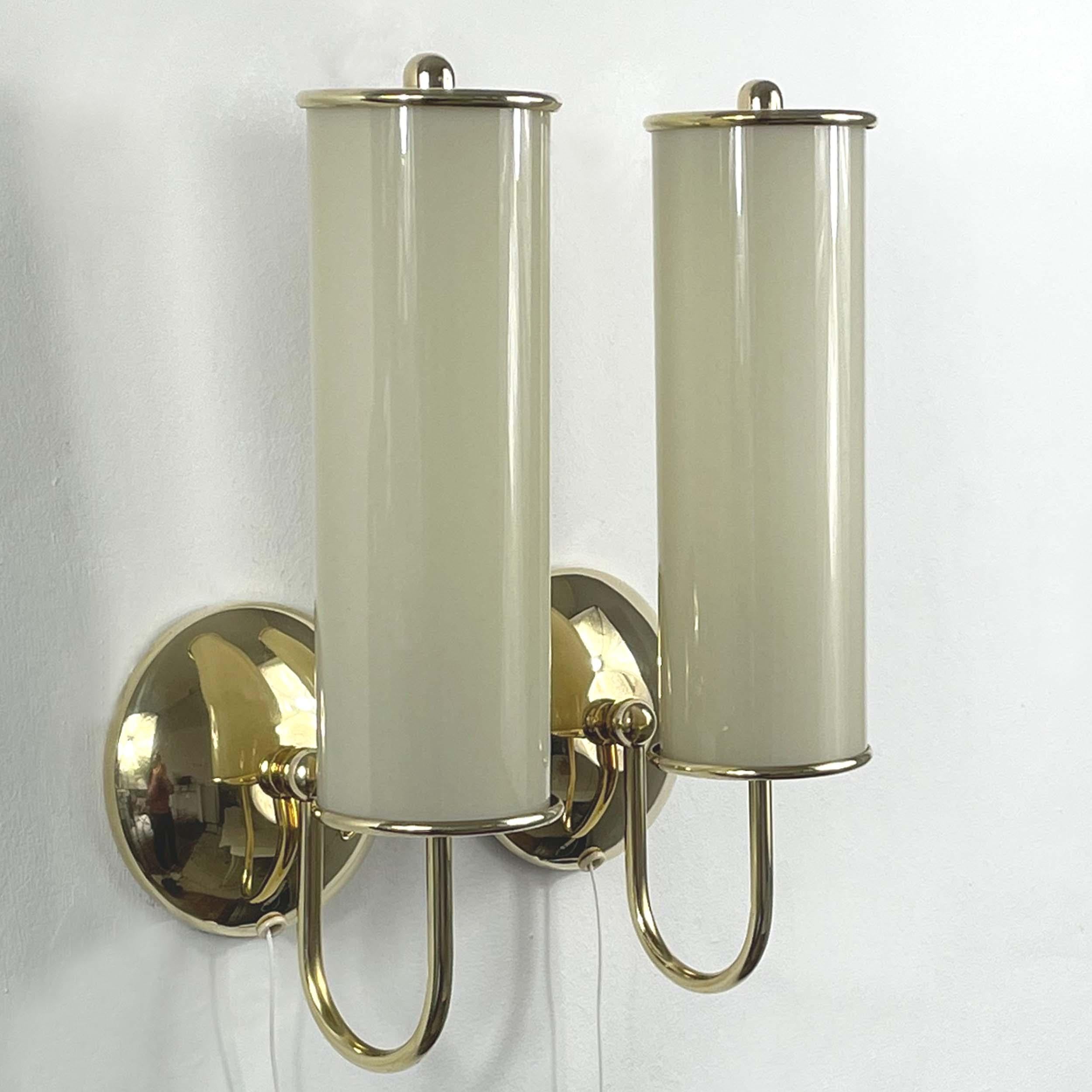 These beautiful wall lights were designed and manufactured in Germany during the Bauhaus period in the 1930s. They feature tube shaped cream colored opaline glass lampshades and brass hardware. 

The sconces have been rewired for use in US and any