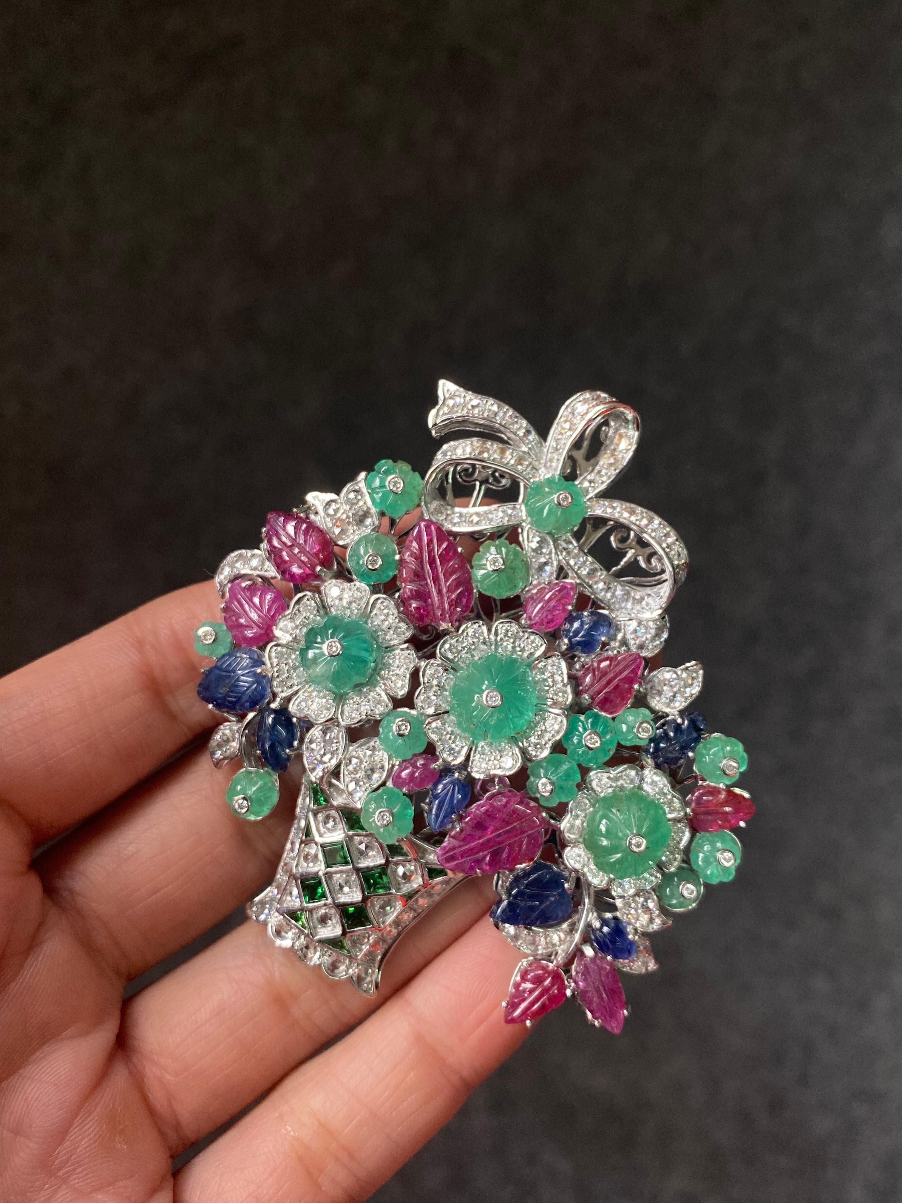 A beautiful art-deco inspired tutti frutti brooch depicting a flower vase, with 11 carat natural Ruby, 6 carat natural Sapphire and 19.2 carat natural Emeralds with 4.3 carats of White Diamonds all set in solid 18K White Gold. 
We provide free