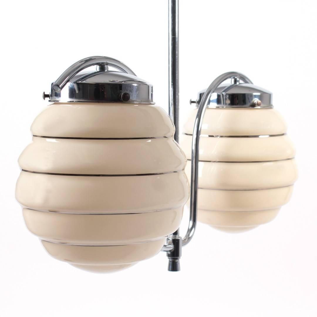 Polished chrome two-arm light fixture with wide-ribbed beige glass shades, USA, circa 1930.

Dimensions:
20 inches L
7 inches W
22 inches H / drop height.