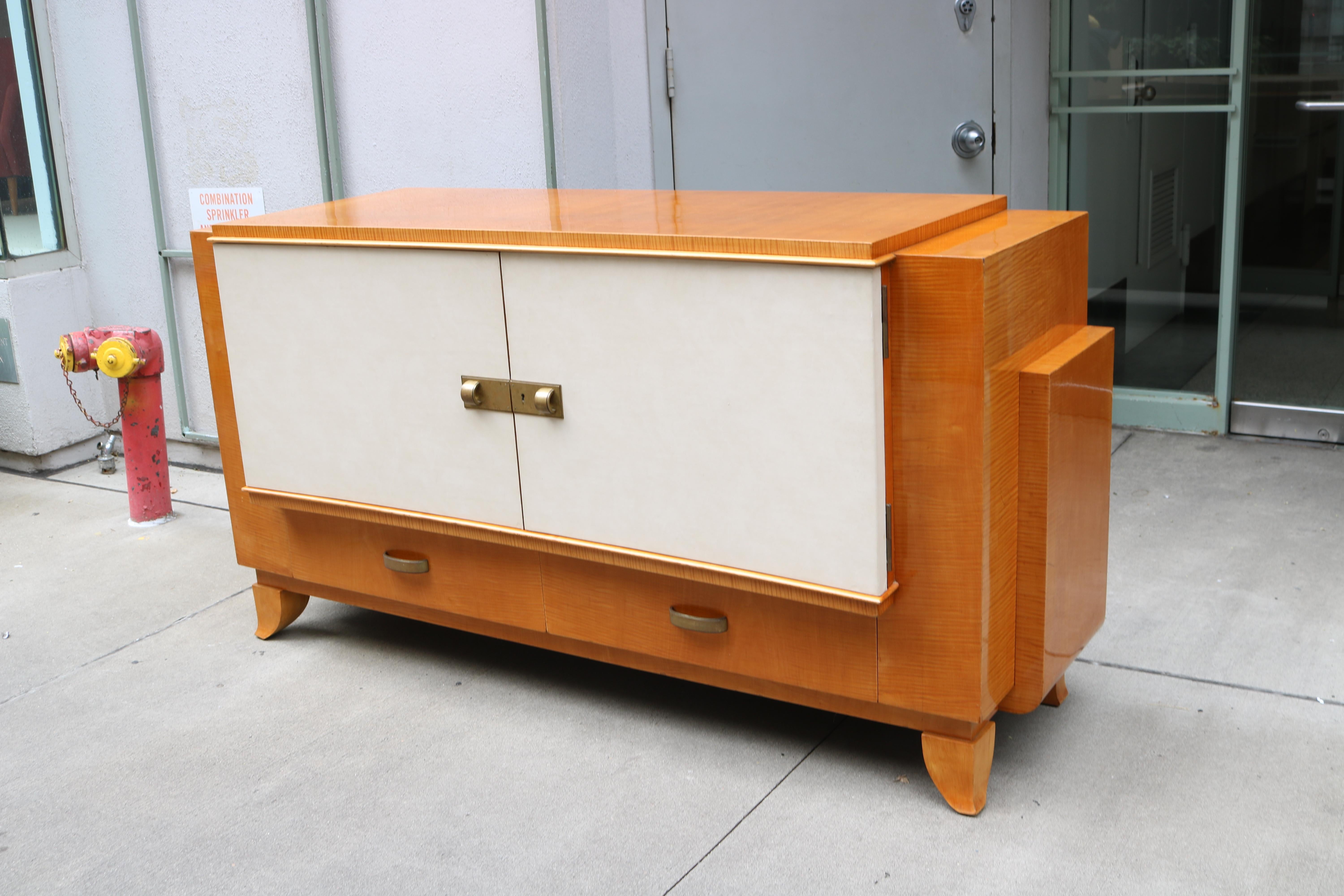 An Art Deco two door sideboard. 
Sycamore with parchment covered doors
and patinated brass pulls and details.