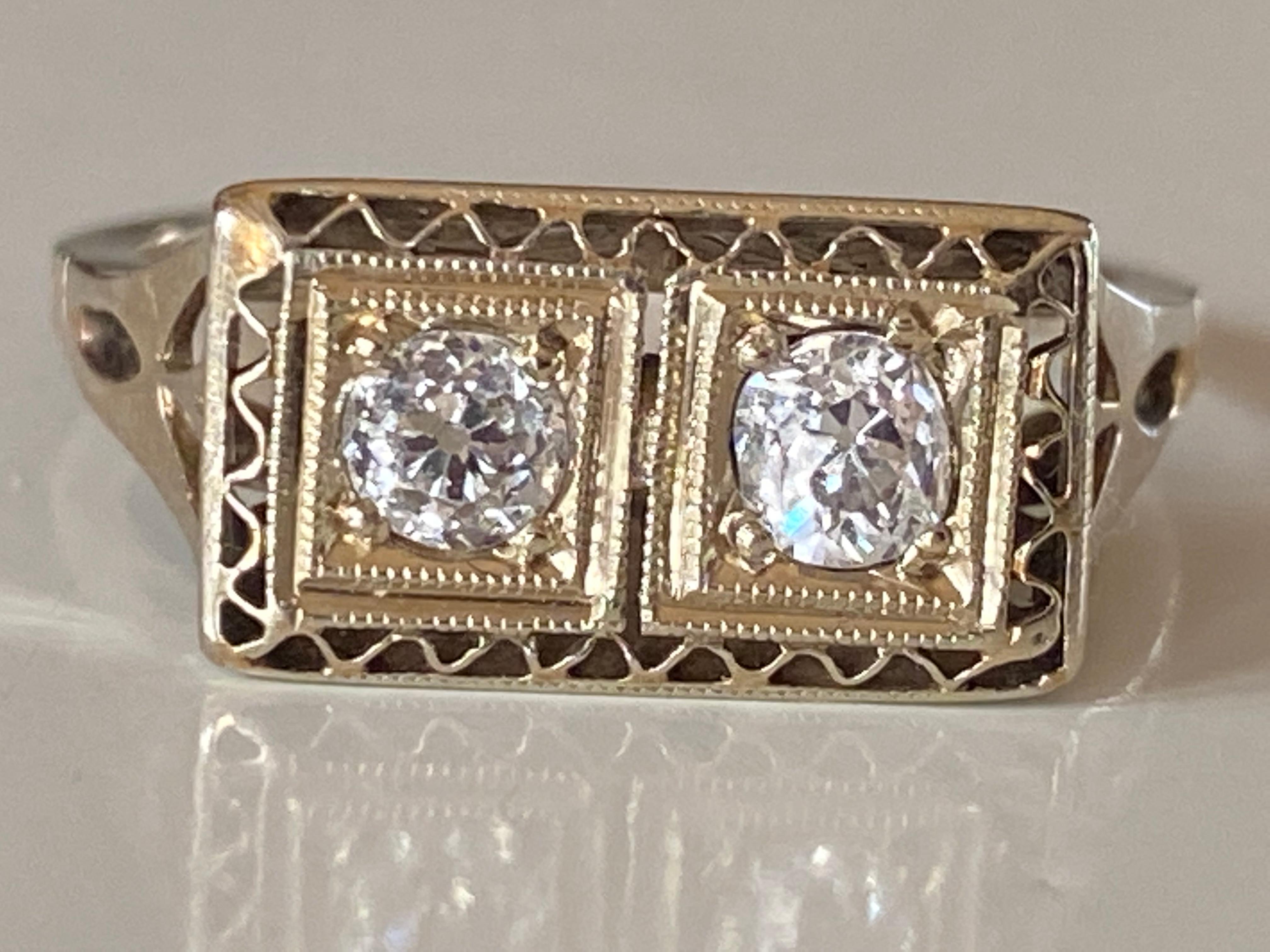 This antique Art Deco ring handcrafted in 14kt white gold features two Old European cut diamonds measuring approximately 0.20 carats each, F color, SI1 clarity, placed side by side and encased in two square frames with delicate milgraining and